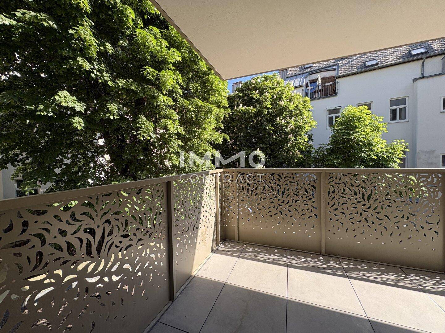 Geräumiger Balkon mit dekorativem Geländer und Fliesenboden, umgeben von grünen Bäumen.