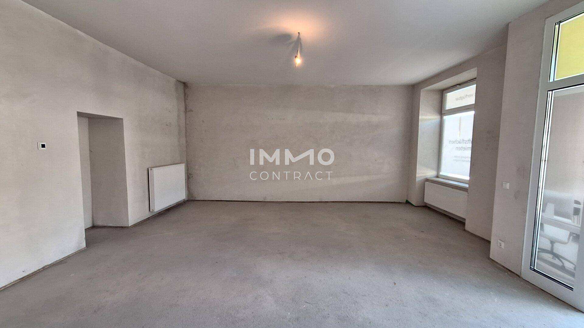 Geräumiger, unmöblierter Raum mit Betonboden, großen Fenstern und einem Heizkörper, bereit für den Ausbau.