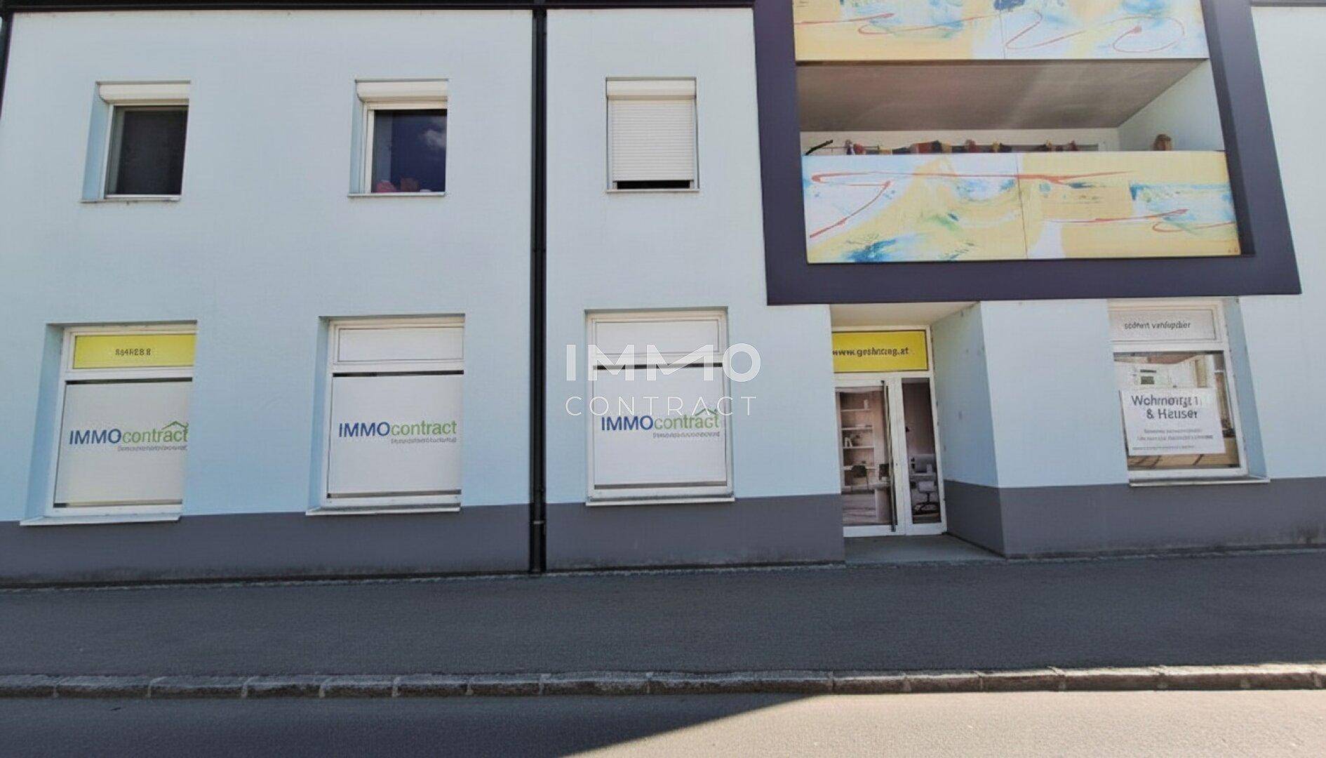 Moderne Gebäudefassade mit großen Fenstern, Rollläden und Geschäftsflächen im Erdgeschoss.