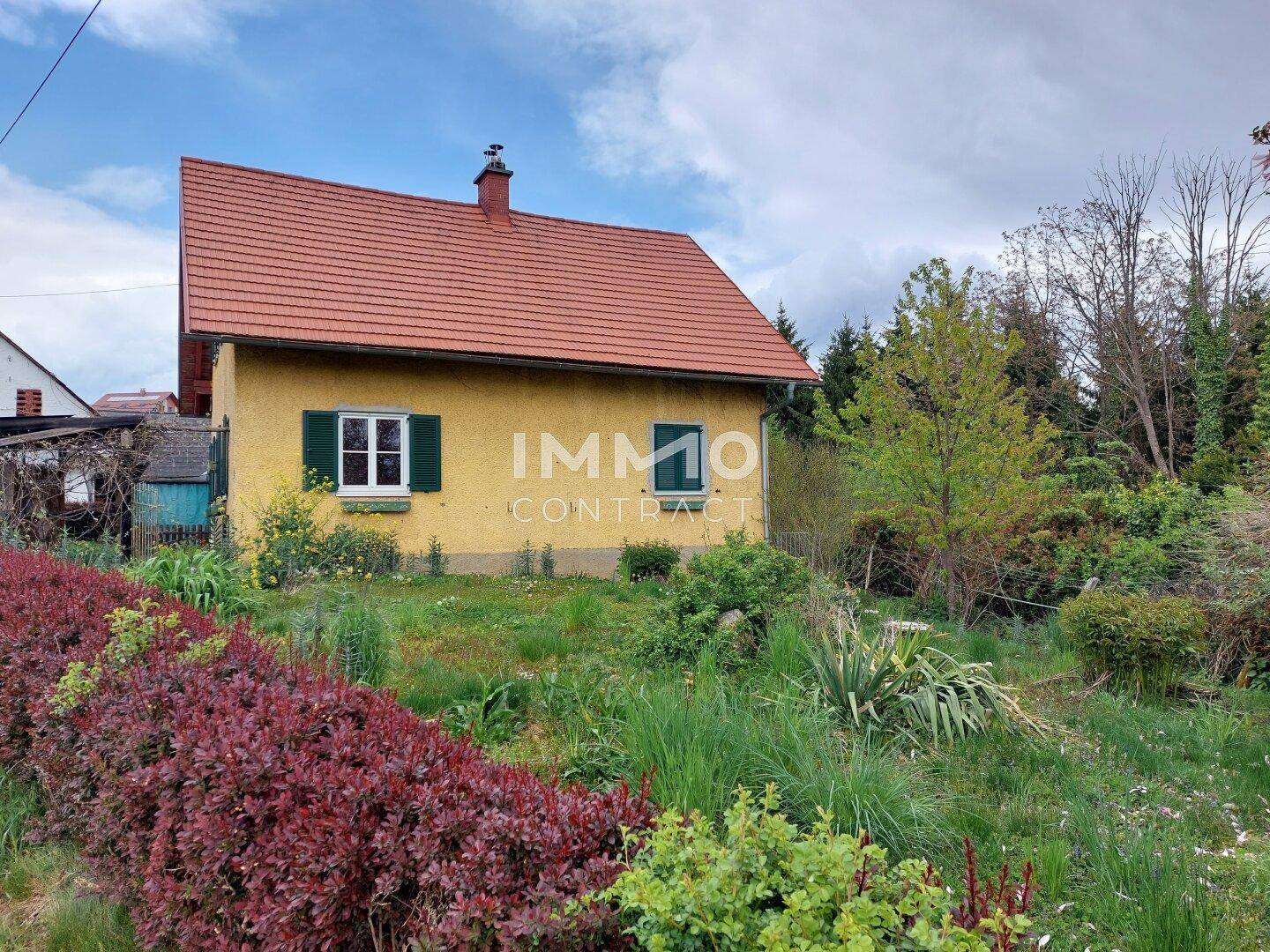 Rückseite des gelben Hauses mit Gartenbereich und Blick auf die umliegende Natur.