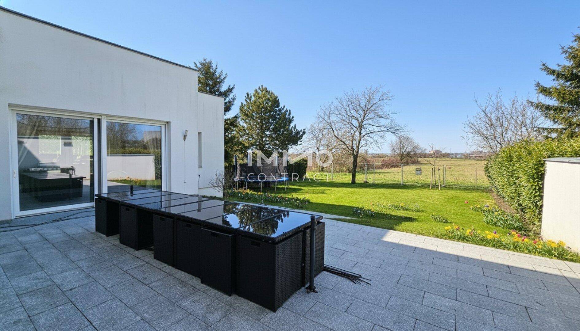 Große gepflasterte Terrasse mit modernen Gartenmöbeln und weitem Blick ins Grüne.