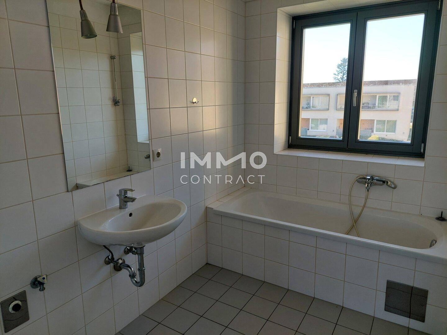 Badezimmer mit weiß gefliesten Wänden, Badewanne, Waschbecken und Fenster.
