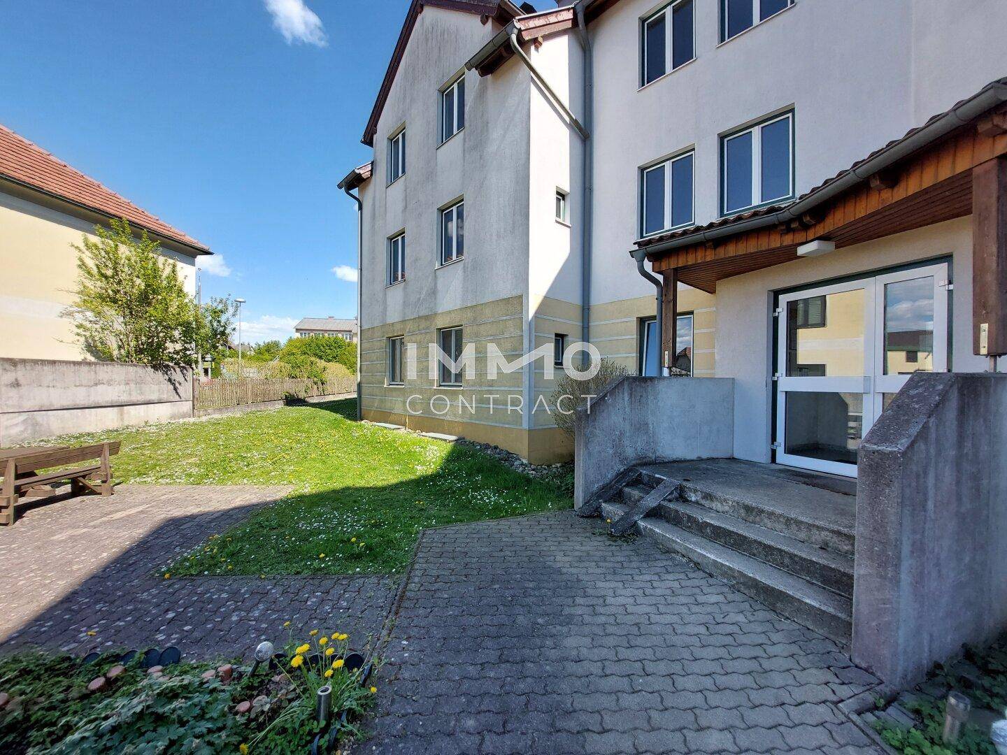 Außenansicht eines Mehrfamilienhauses mit Eingangsbereich, Treppe und Rasenfläche.