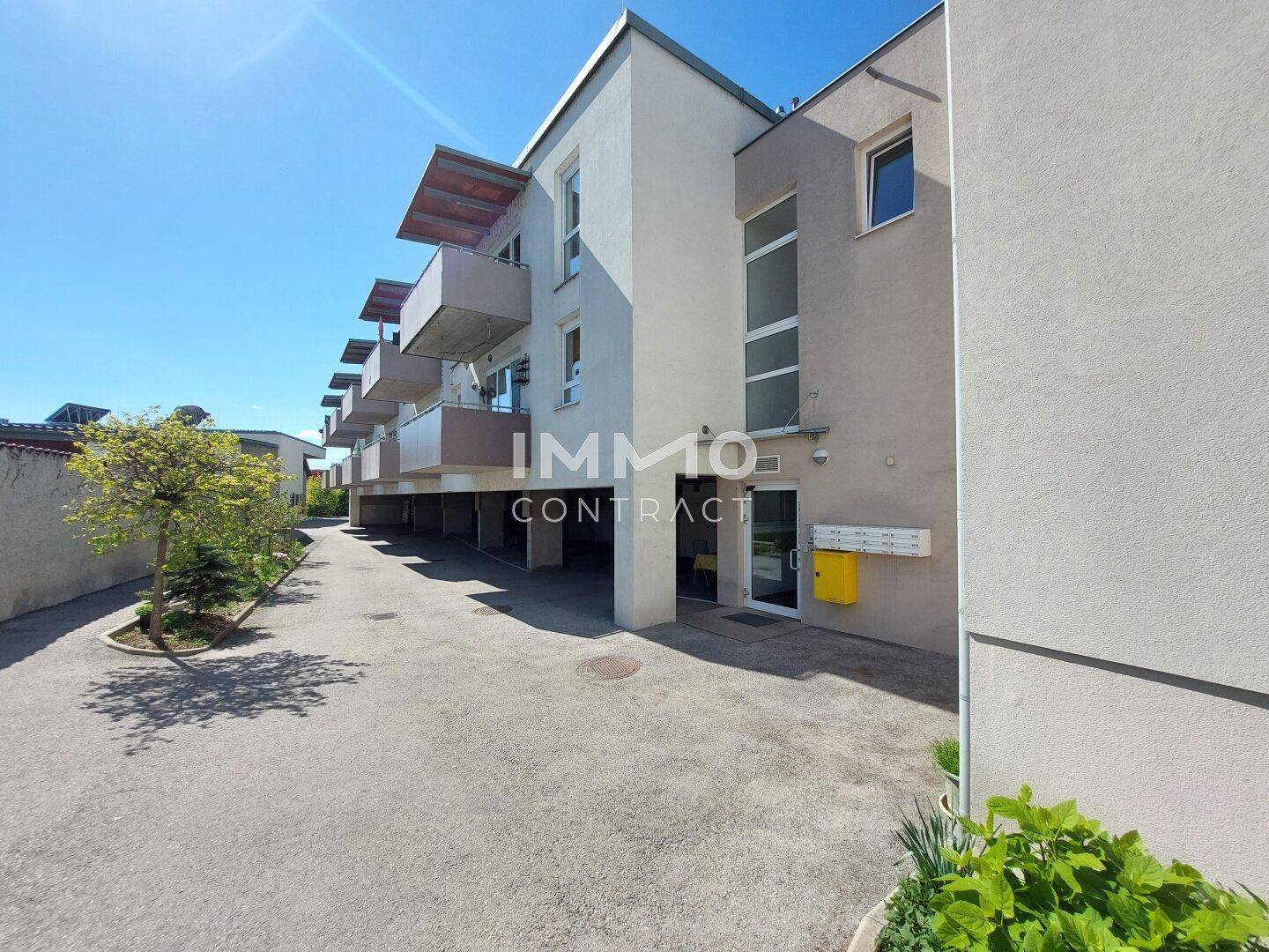 Modernes Mehrfamilienhaus mit Balkonen und Zufahrt an einem sonnigen Tag.