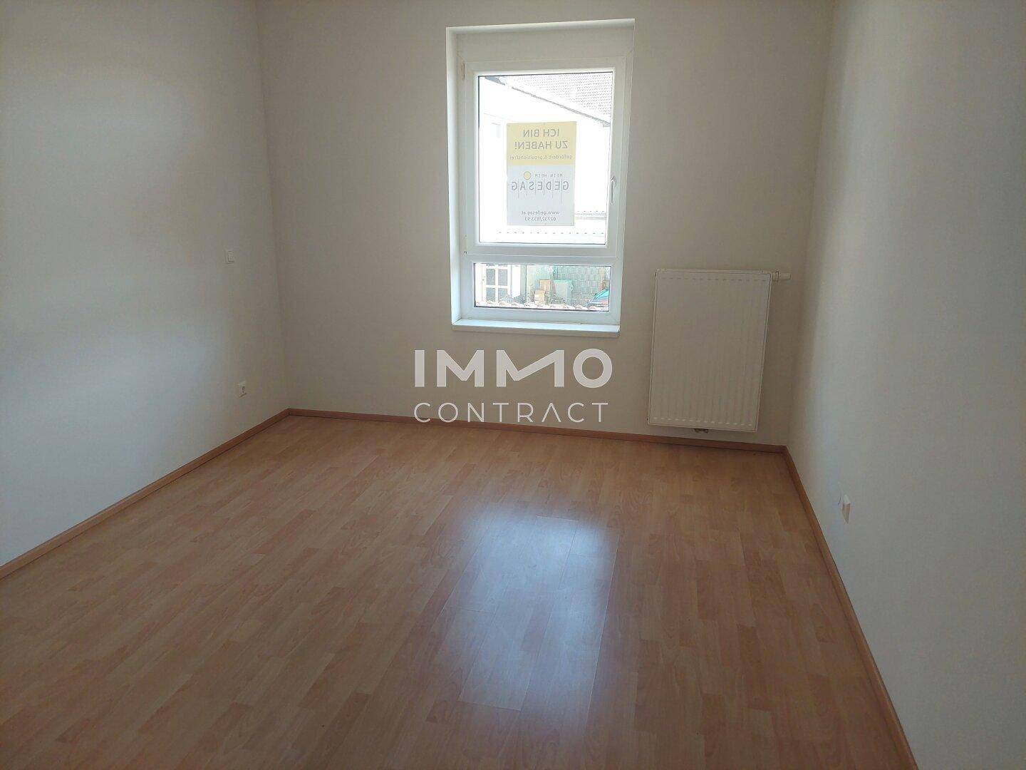 Helles Zimmer mit Fenster und Heizkörper, ausgestattet mit Laminatboden.