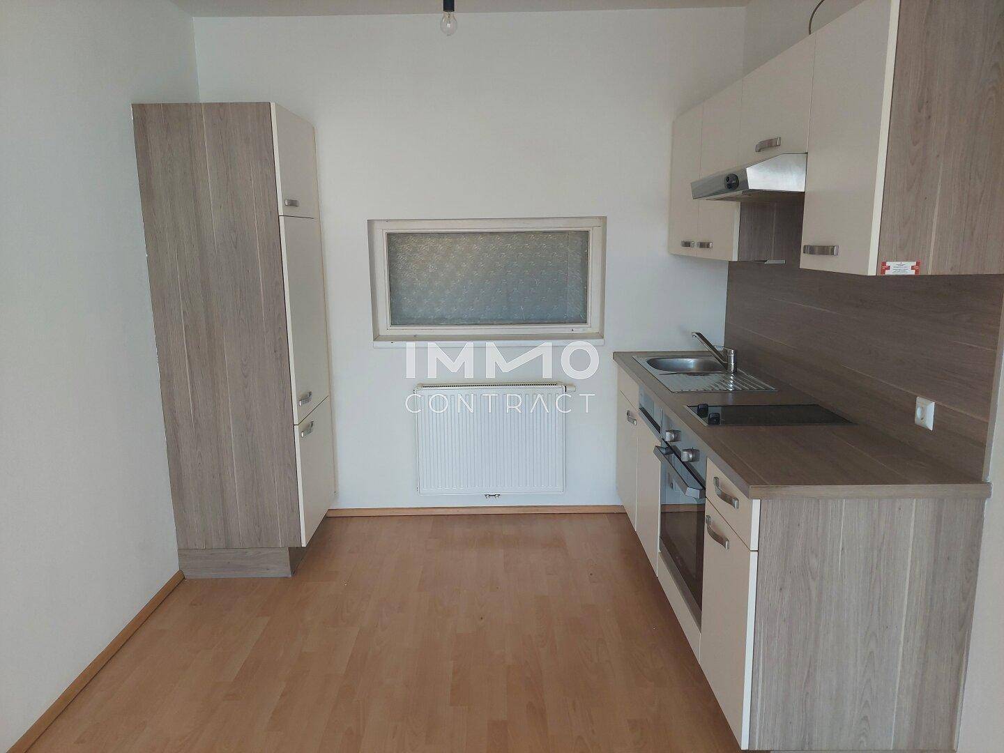 Moderne Küchenzeile mit hellen Fronten, integriertem Backofen und Fenster.