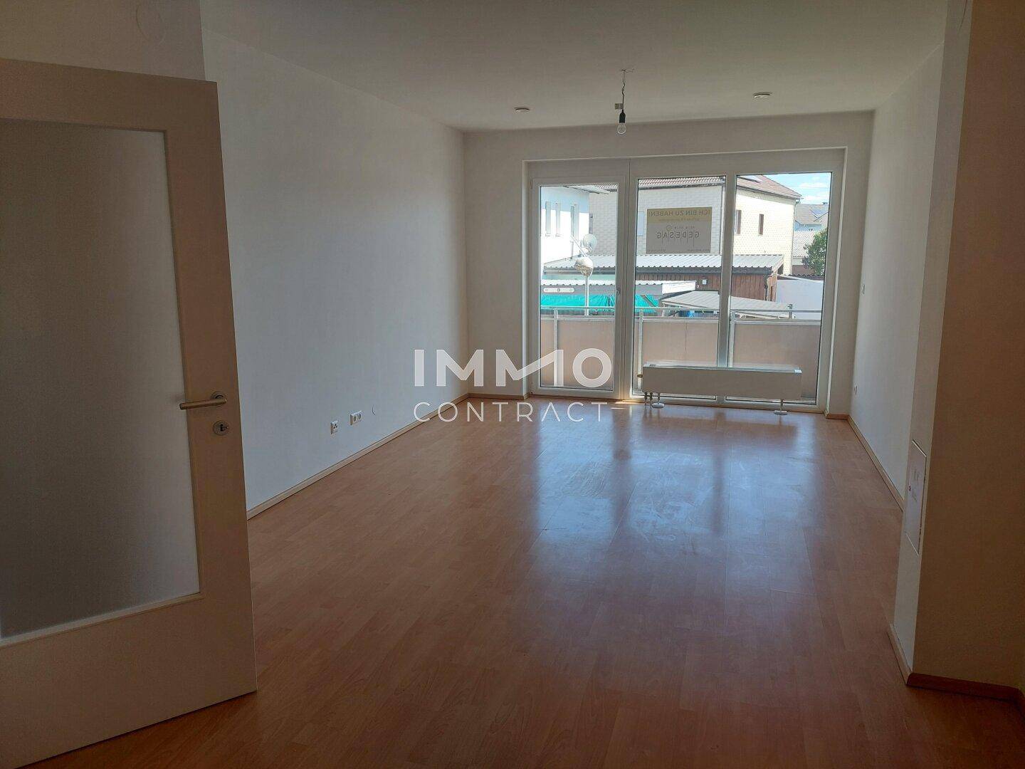 Geräumiges Wohnzimmer mit Zugang zu einem Balkon und hellem Laminatboden.