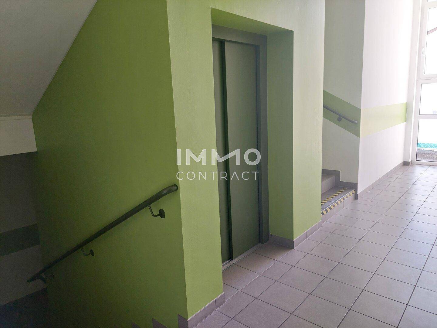 Treppenhaus mit Aufzug und Fliesenboden in einem Mehrparteienhaus.