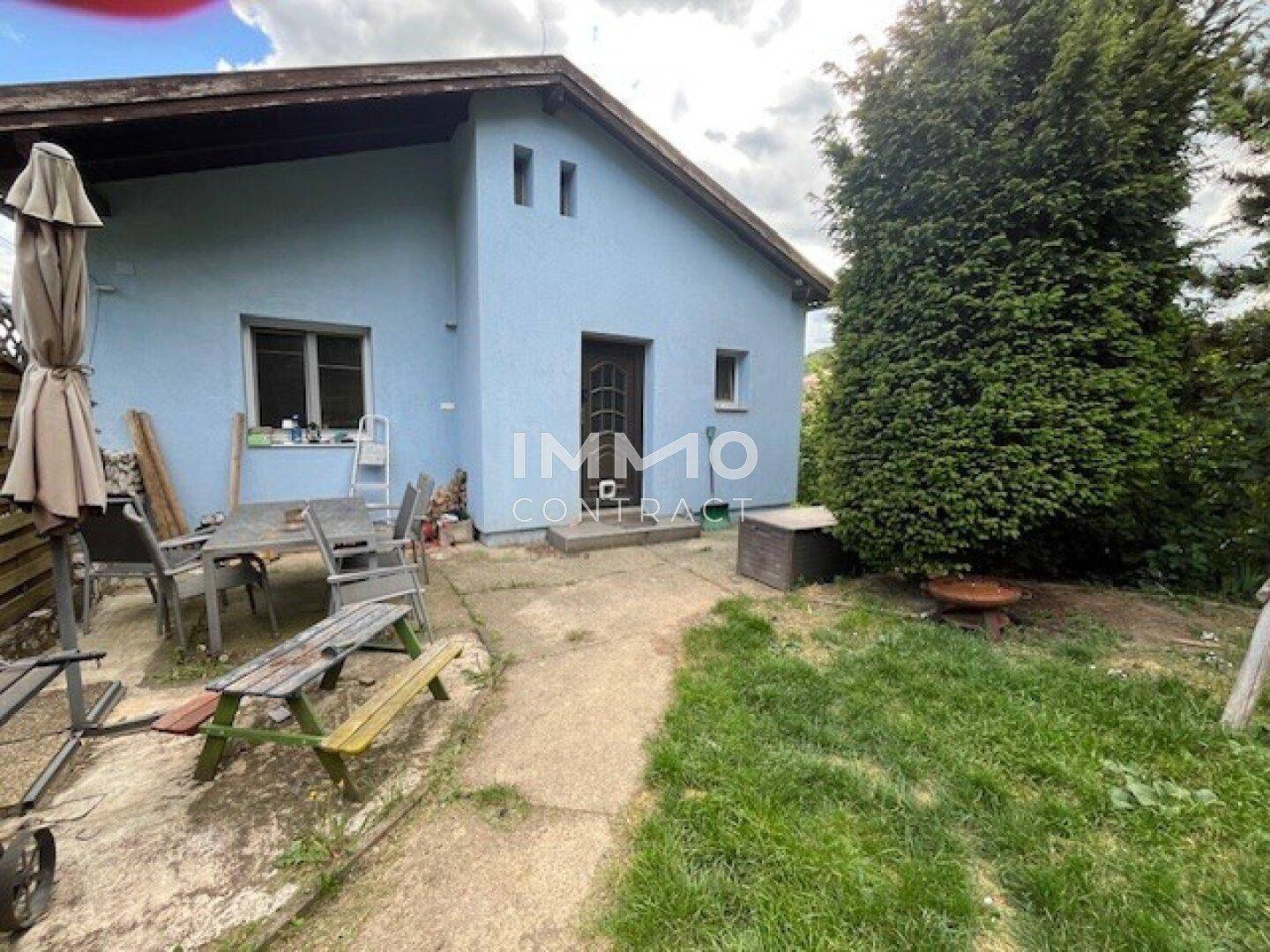 Rückseite des blauen Hauses mit einer möblierten Terrasse und einer kleinen Rasenfläche.