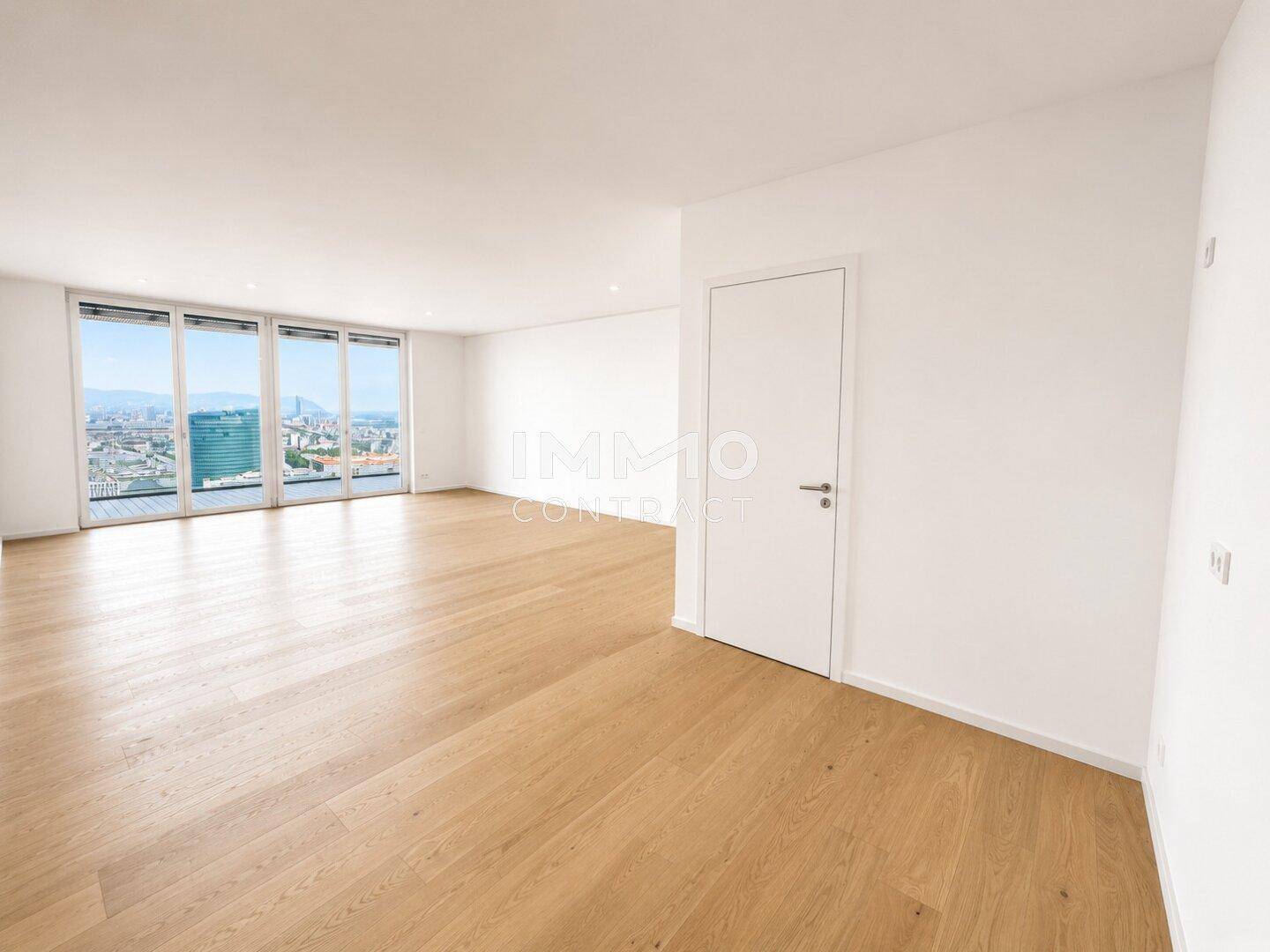 Helles, leeres Wohnzimmer mit Eichenparkettboden und großen Fenstern, die einen weiten Stadtblick bieten.