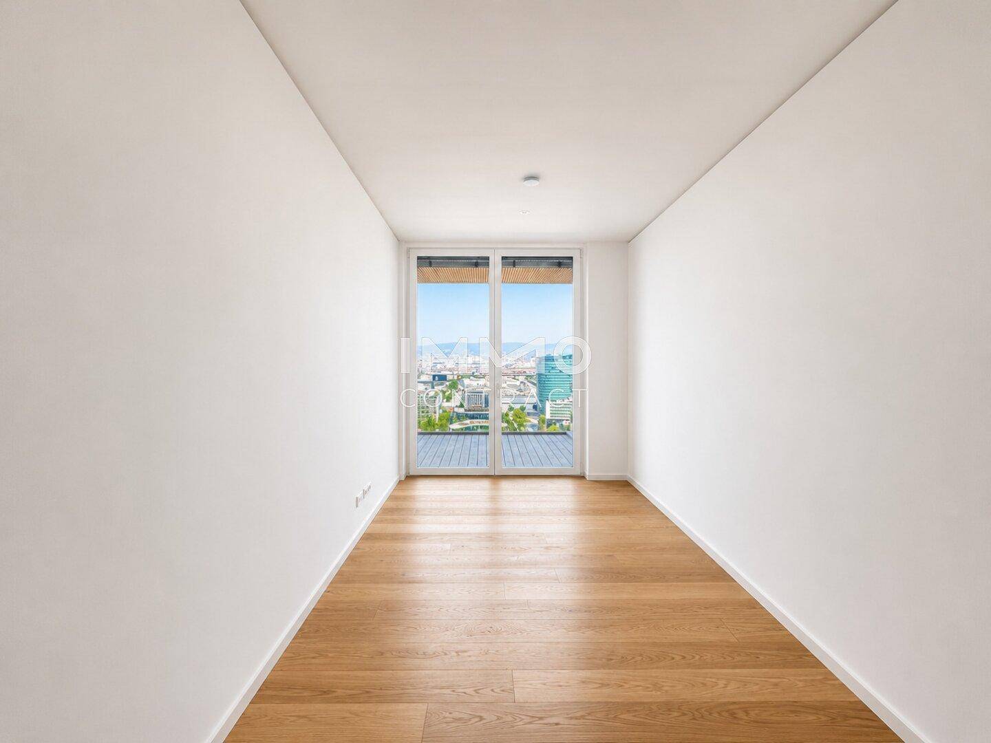 Leeres Zimmer mit Eichenparkettboden und Zugang zu einem Balkon mit Stadtblick.