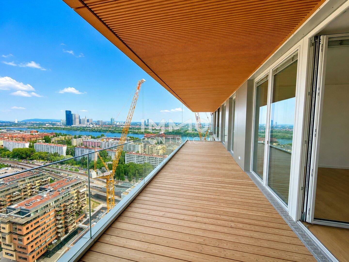 Breiter Holzbalkon mit Glasgeländer und weitem Blick über die Stadt und den Fluss.