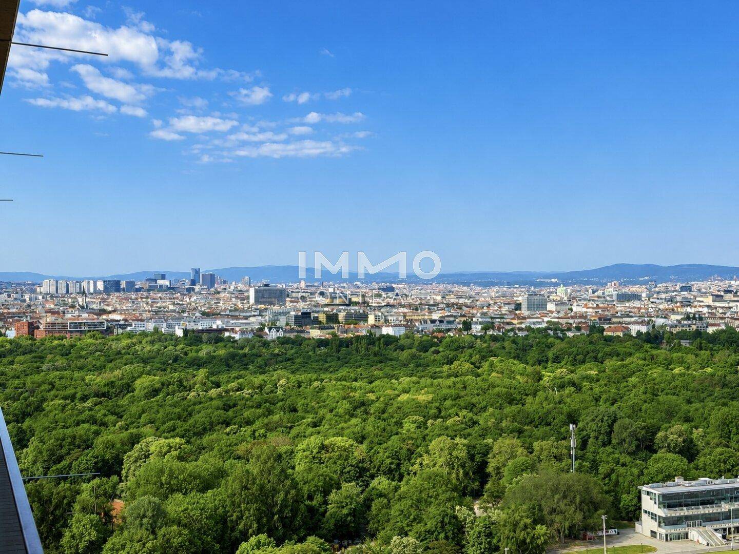 Panoramablick über die Stadt mit ausgedehnten Grünflächen und Bergen im Hintergrund.
