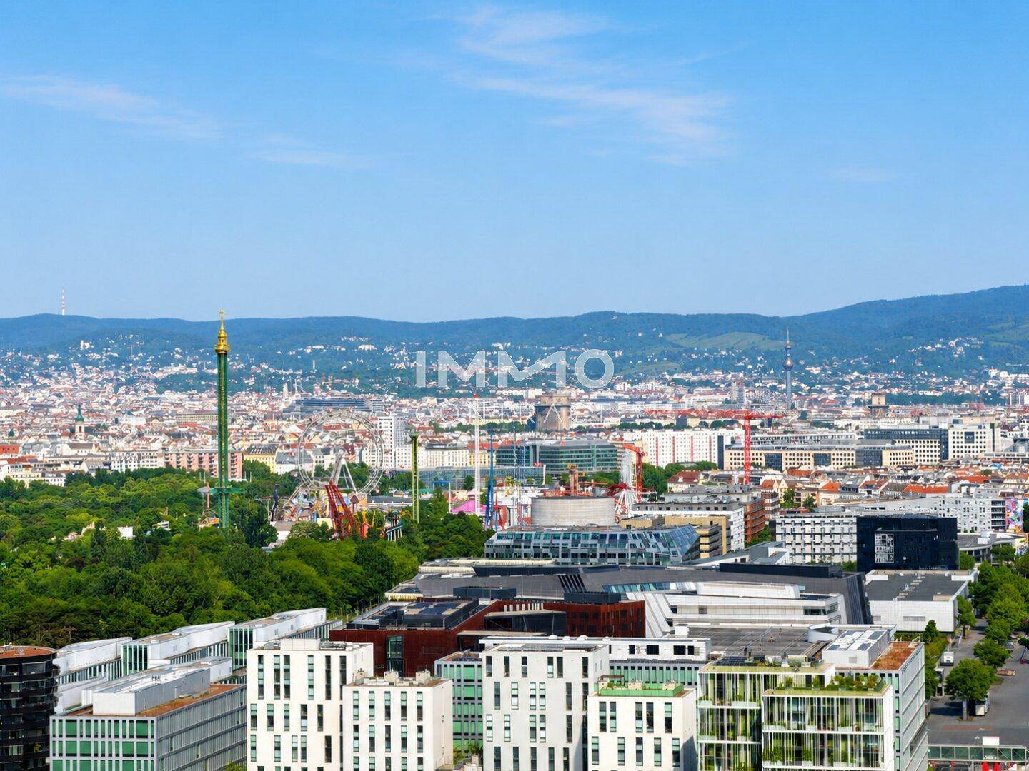 Panoramablick über die Stadt mit vielen Gebäuden, Grünflächen und Bergen im Hintergrund.