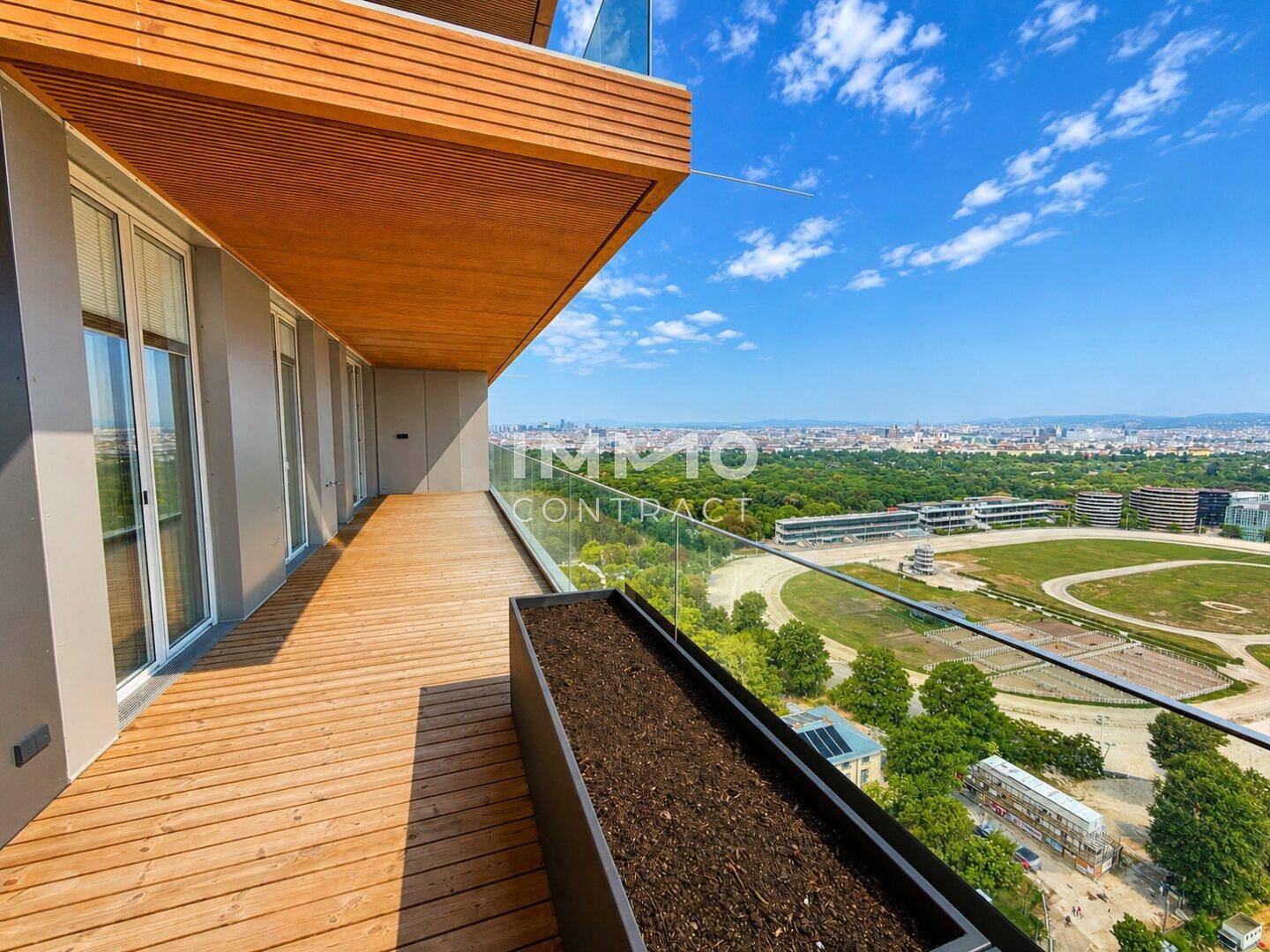 Geräumiger Balkon mit Holzboden und Pflanzkübel, bietet einen Panoramablick über die Stadt und Grünflächen.