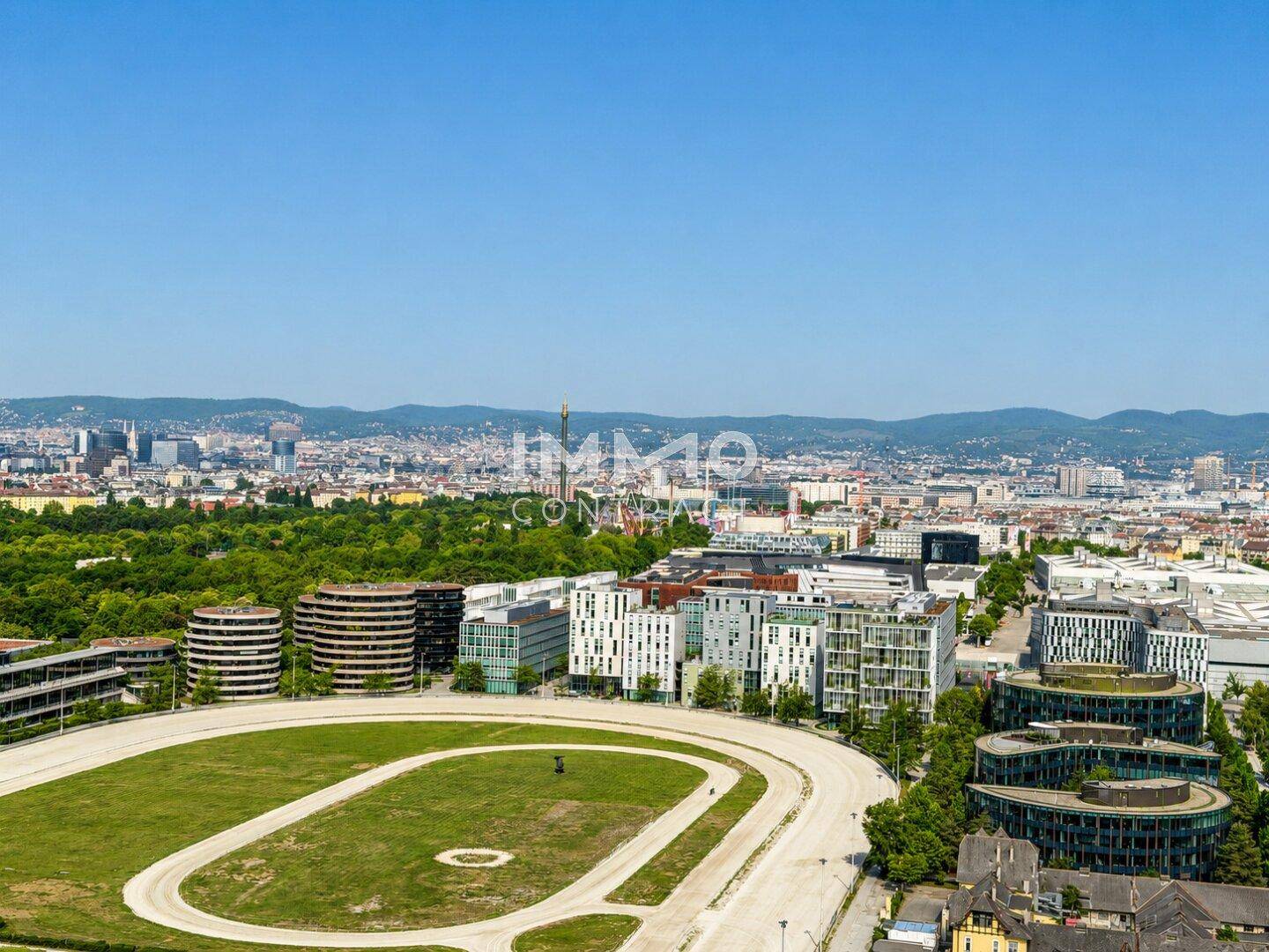 Weitläufiger Blick über eine Pferderennbahn und die moderne Stadtlandschaft im Sonnenschein.