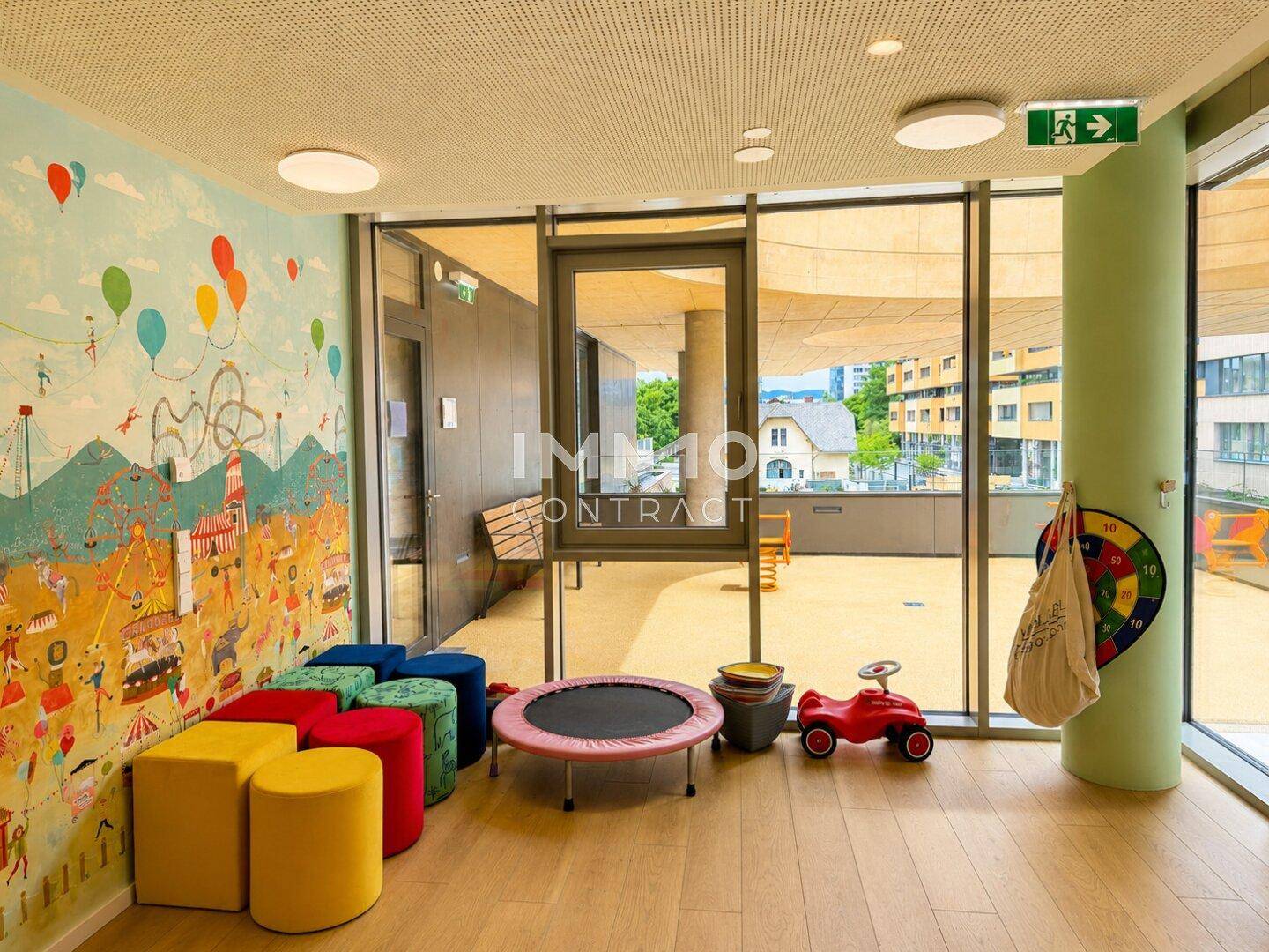 Farbenfroher Kinderspielbereich mit Wandmalerei, Trampolin und Zugang zu einer Außenterrasse.