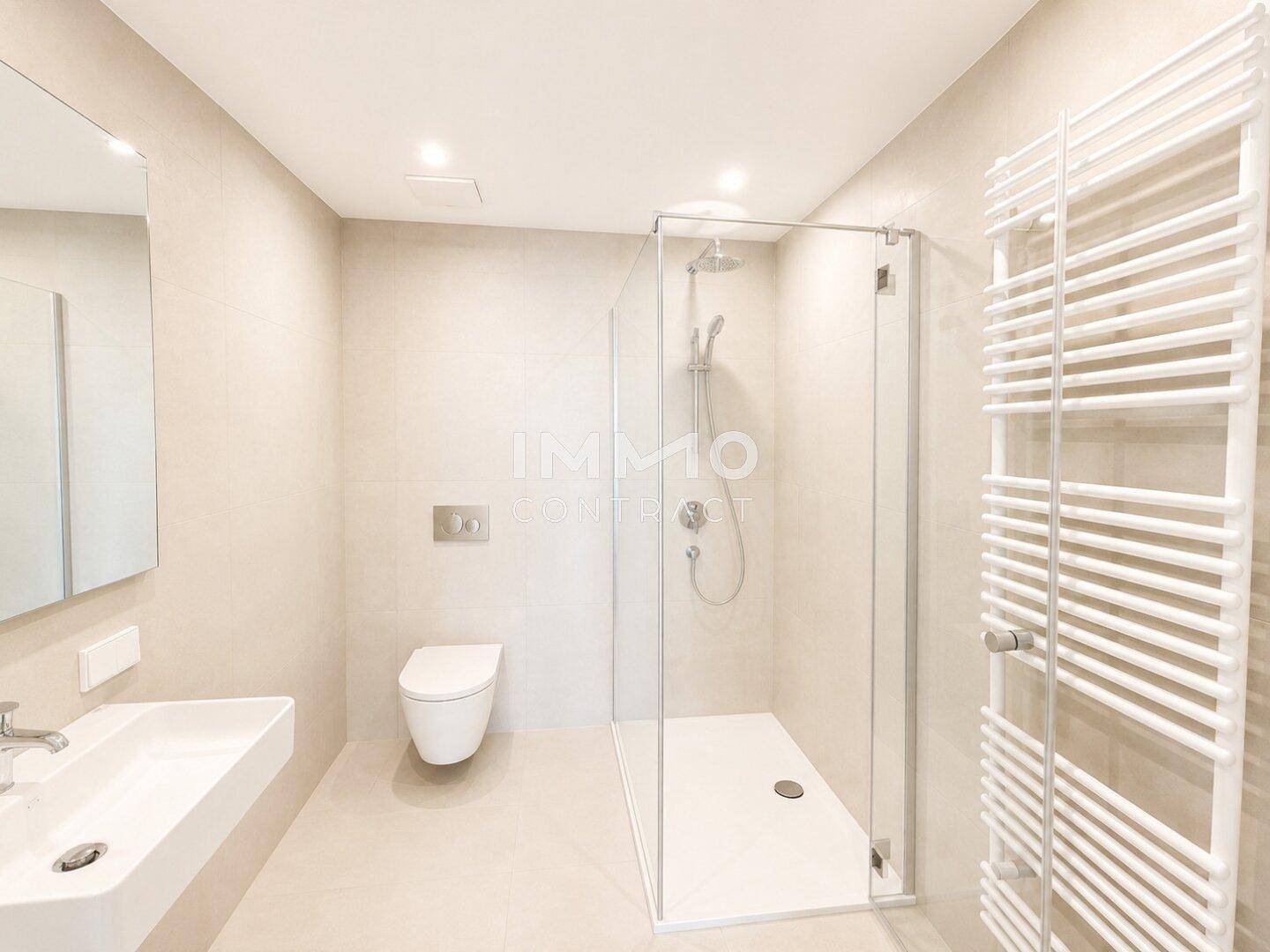 Modernes Badezimmer mit beigefarbenen Fliesen, wandhängendem WC, Dusche und Handtuchheizkörper.