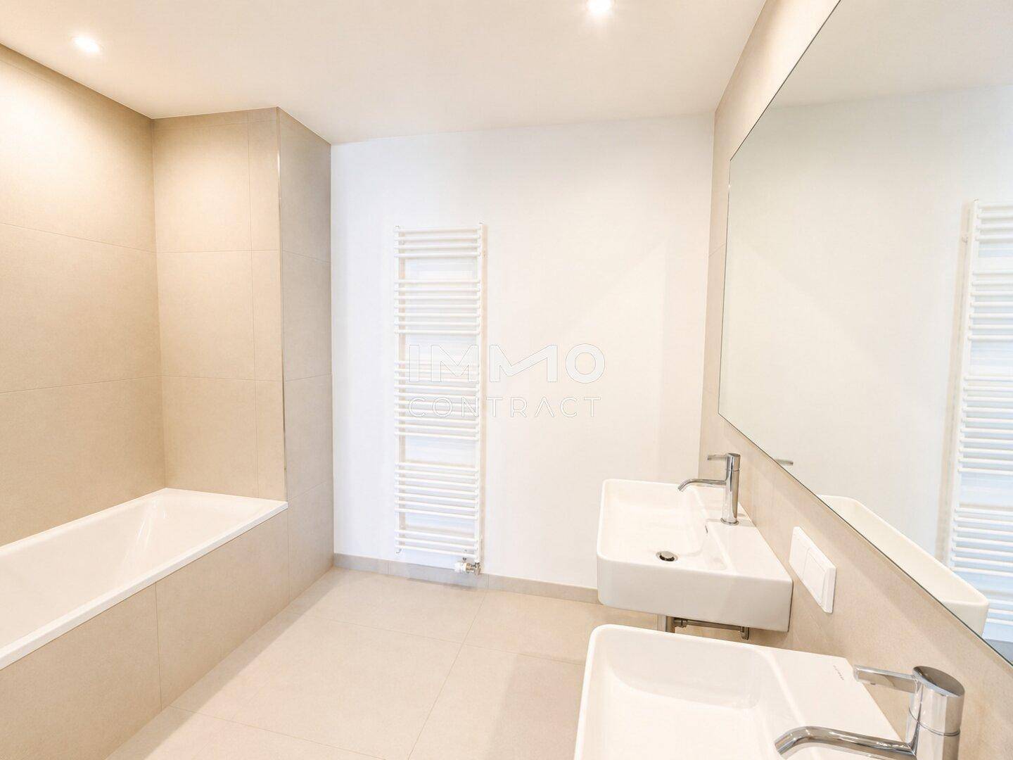 Modernes Badezimmer mit Doppelwaschbecken, Badewanne, beigefarbenen Fliesen und großem Spiegel.