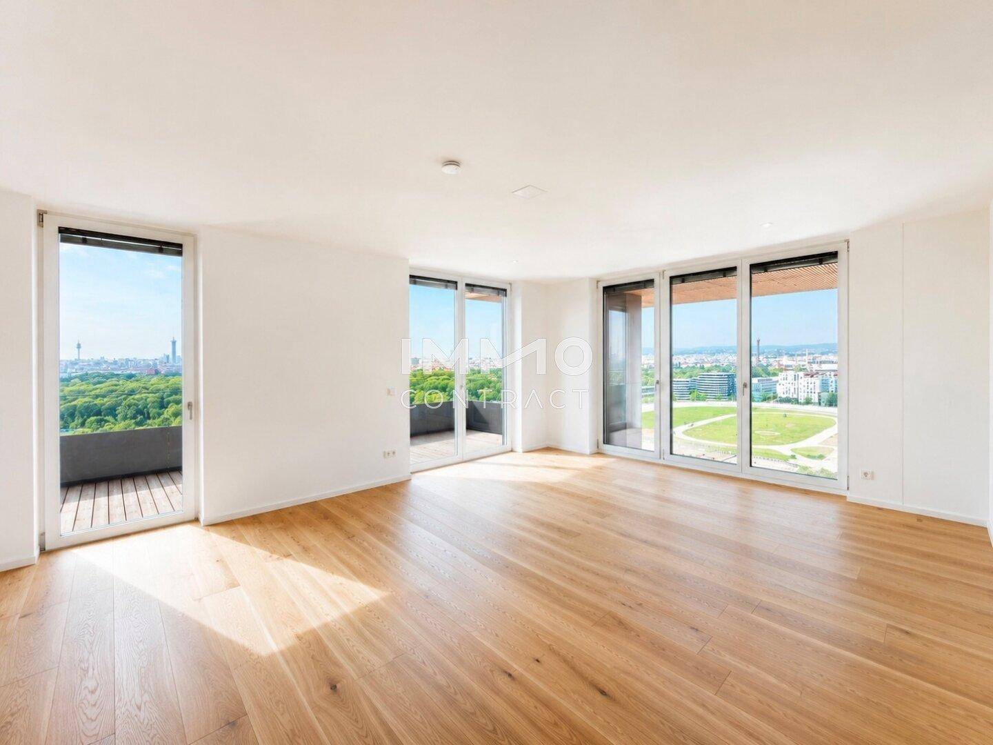 Helles, leeres Wohnzimmer mit großen Fenstern, Holzboden und Zugang zu einem Balkon.