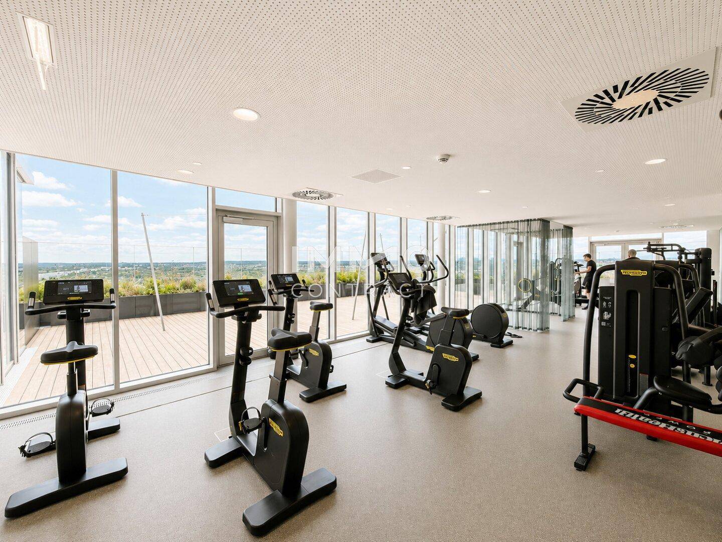 Gut ausgestatteter Fitnessraum mit modernen Geräten und großen Fenstern, die einen Panoramablick bieten.