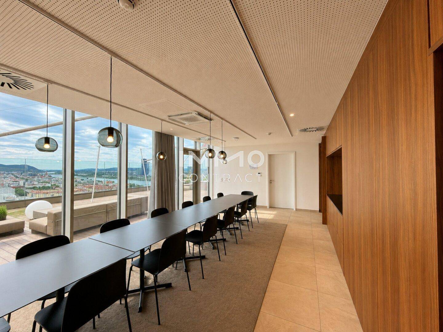 Moderner Konferenzraum mit langem Tisch, Stühlen und großen Fenstern mit Stadtblick.