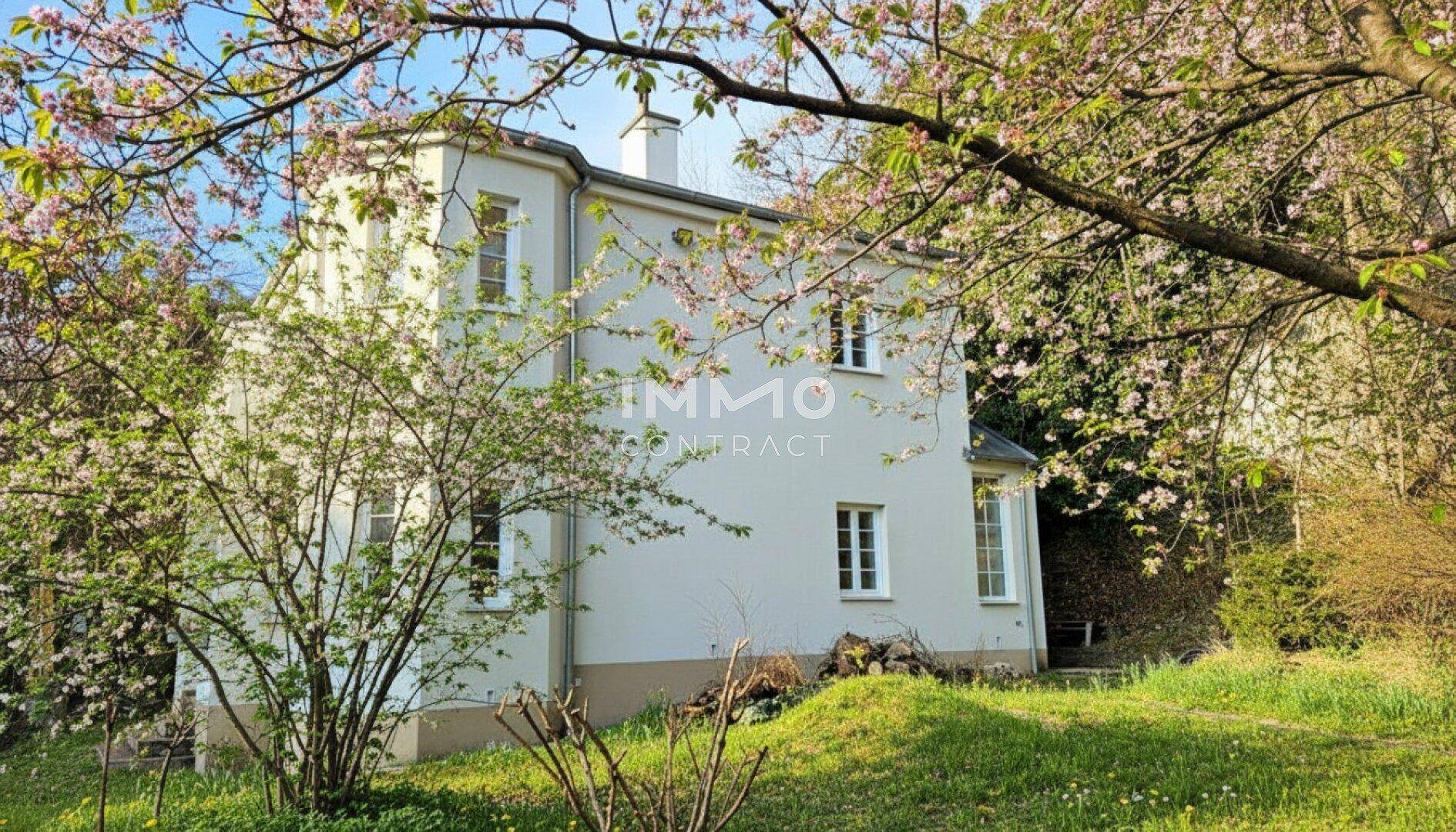Charmantes weißes Haus umgeben von blühenden Bäumen und üppigem Grün.