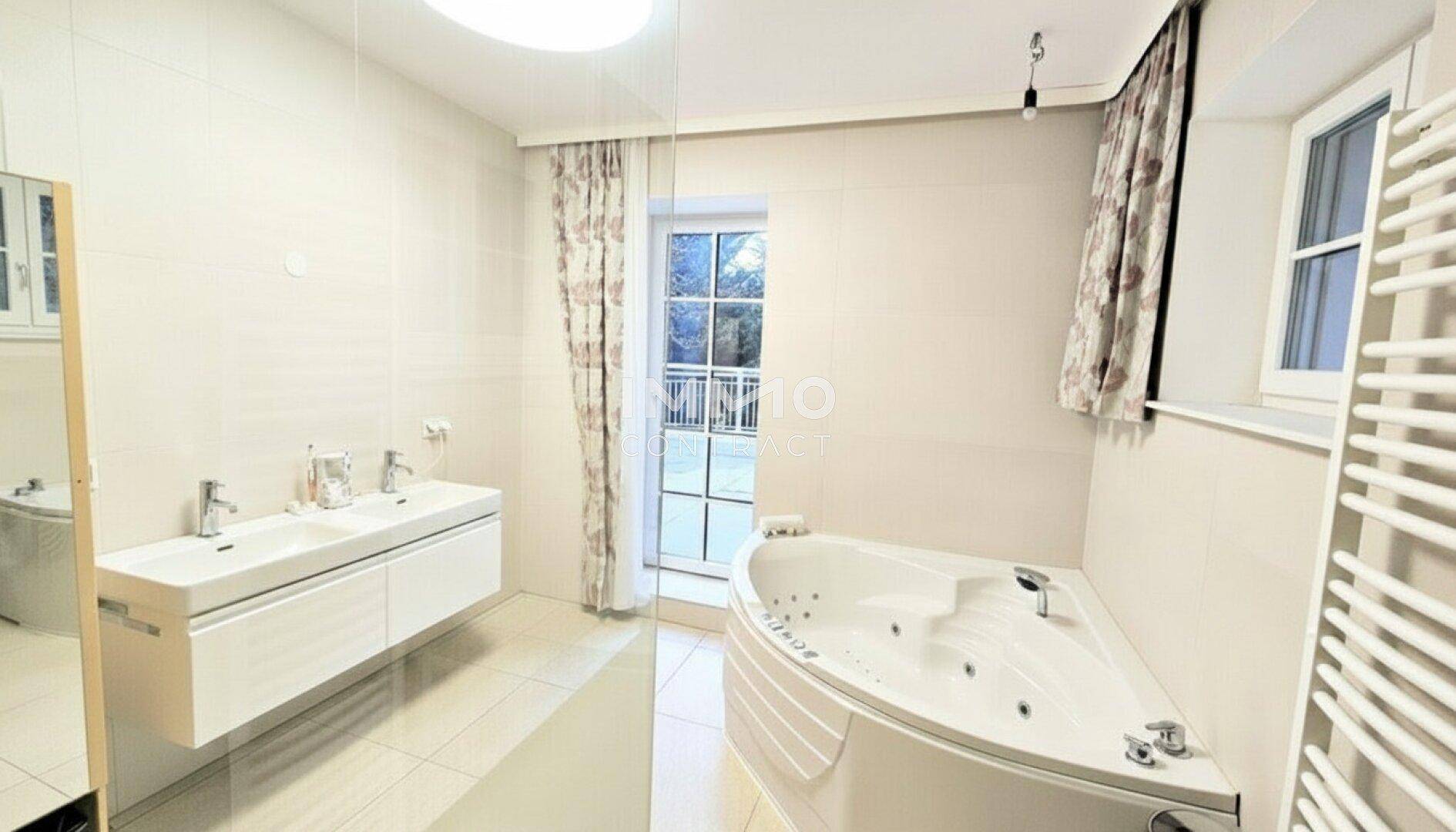 Modernes Badezimmer mit Doppelwaschbecken, Eck-Whirlpool und Zugang zu einem Balkon.