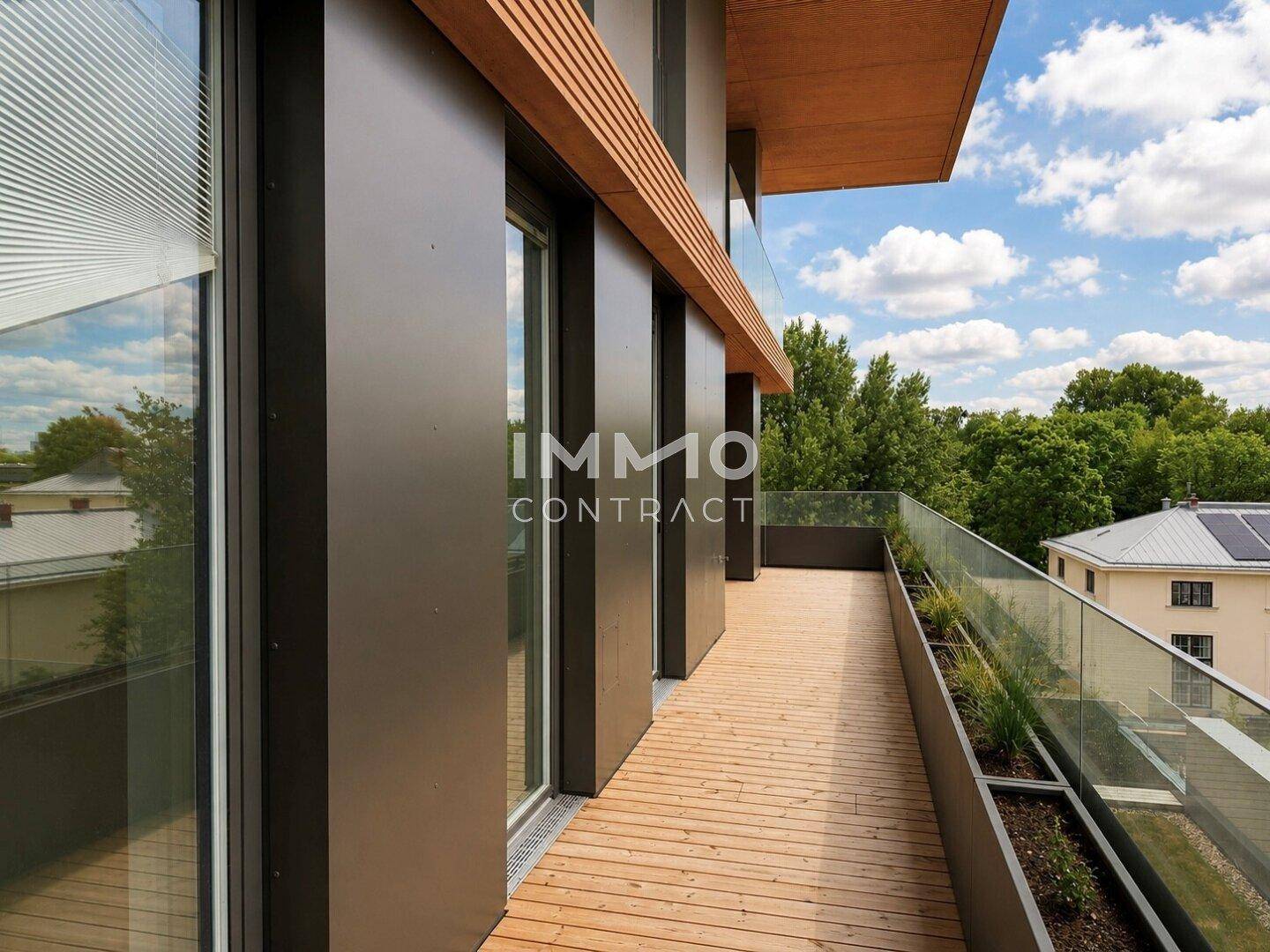 Langer Balkon mit Holzbelag, Glasgeländer und integrierten Pflanzgefäßen.