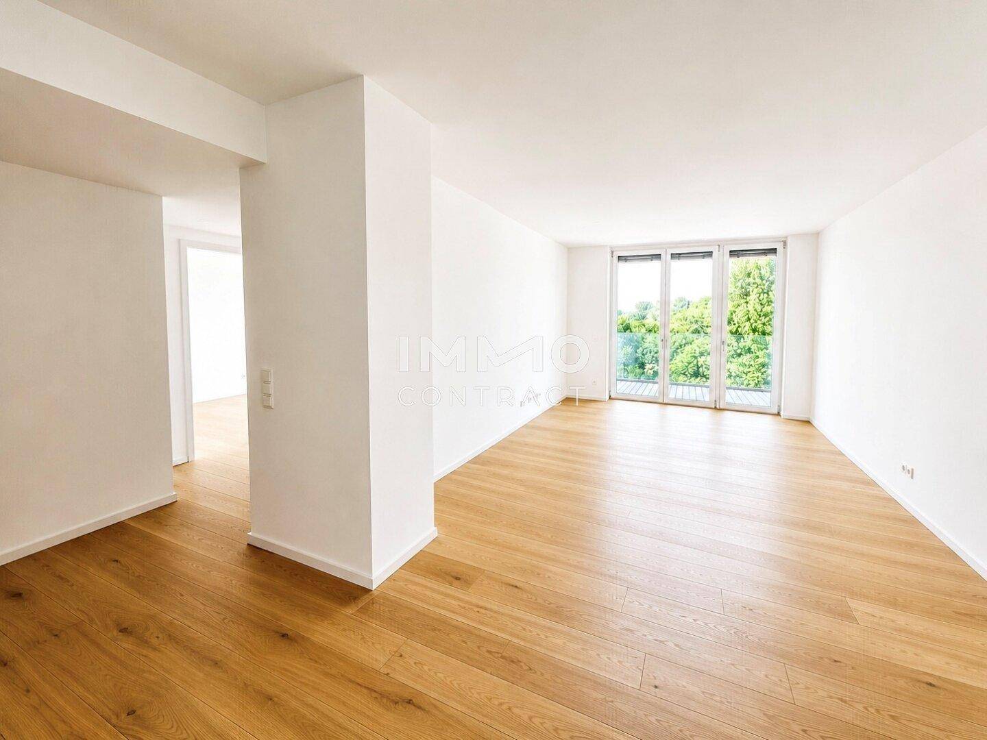 Geräumiger, heller Wohnbereich mit Holzboden und großen Fenstern mit Blick ins Grüne.