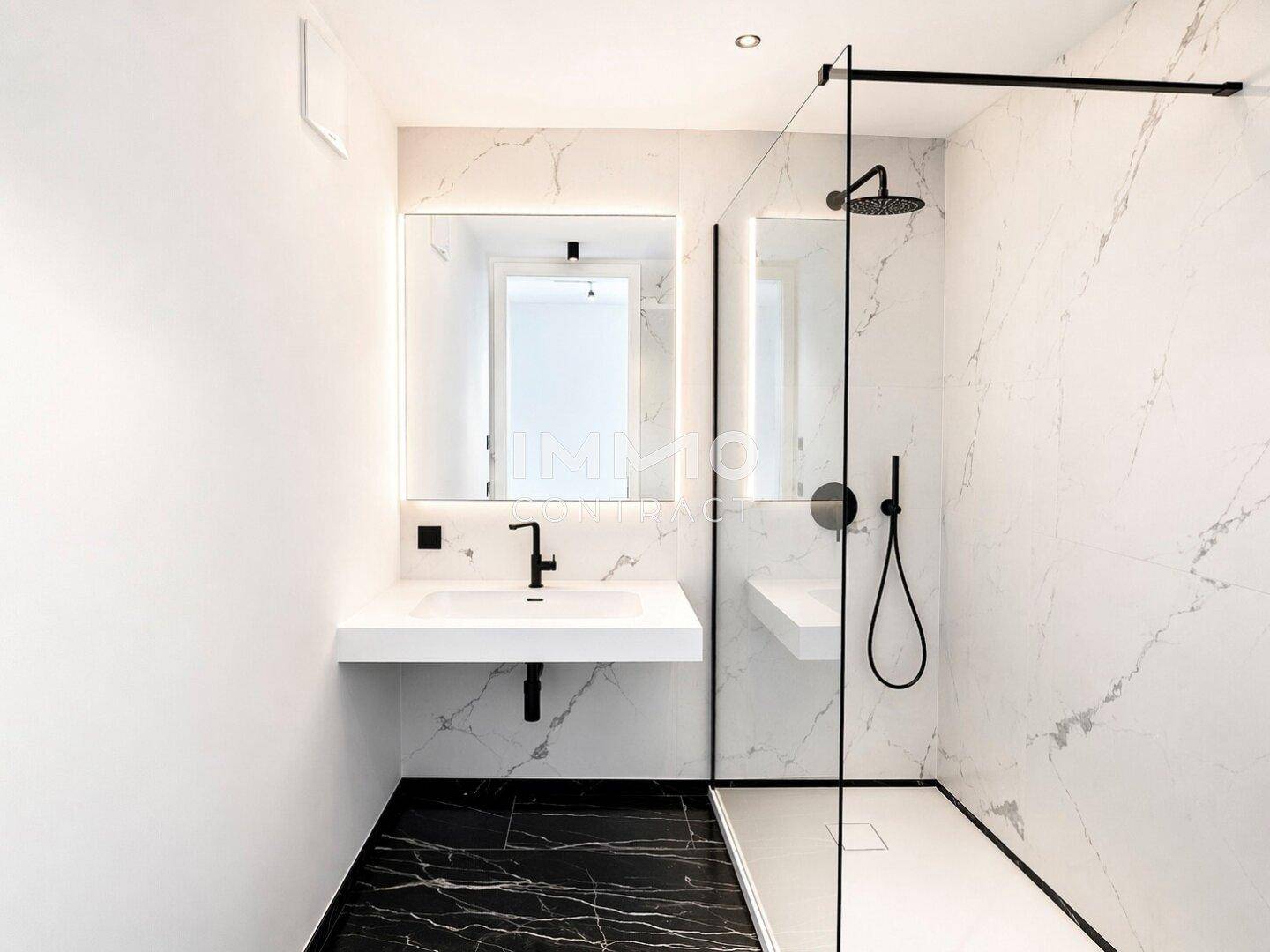 Modernes Badezimmer mit weißem Marmor und schwarzem Boden, bodengleicher Dusche und minimalistischem Waschtisch.