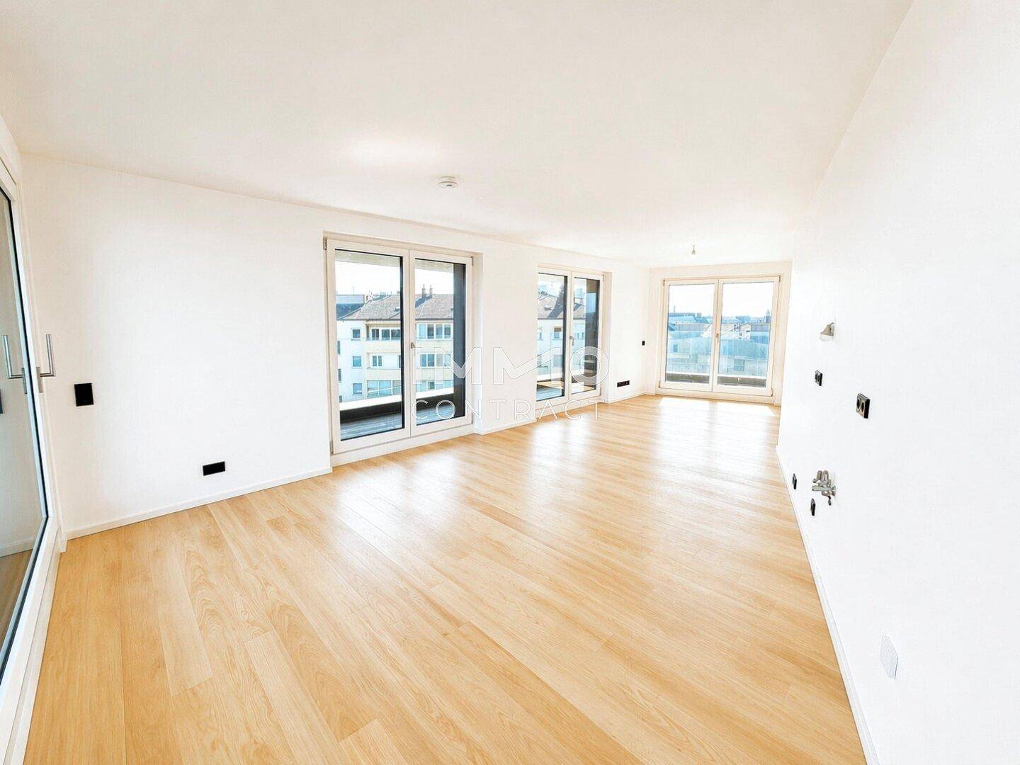 Geräumiges Wohnzimmer mit hellem Holzparkettboden und mehreren großen Fenstern mit Stadtblick.