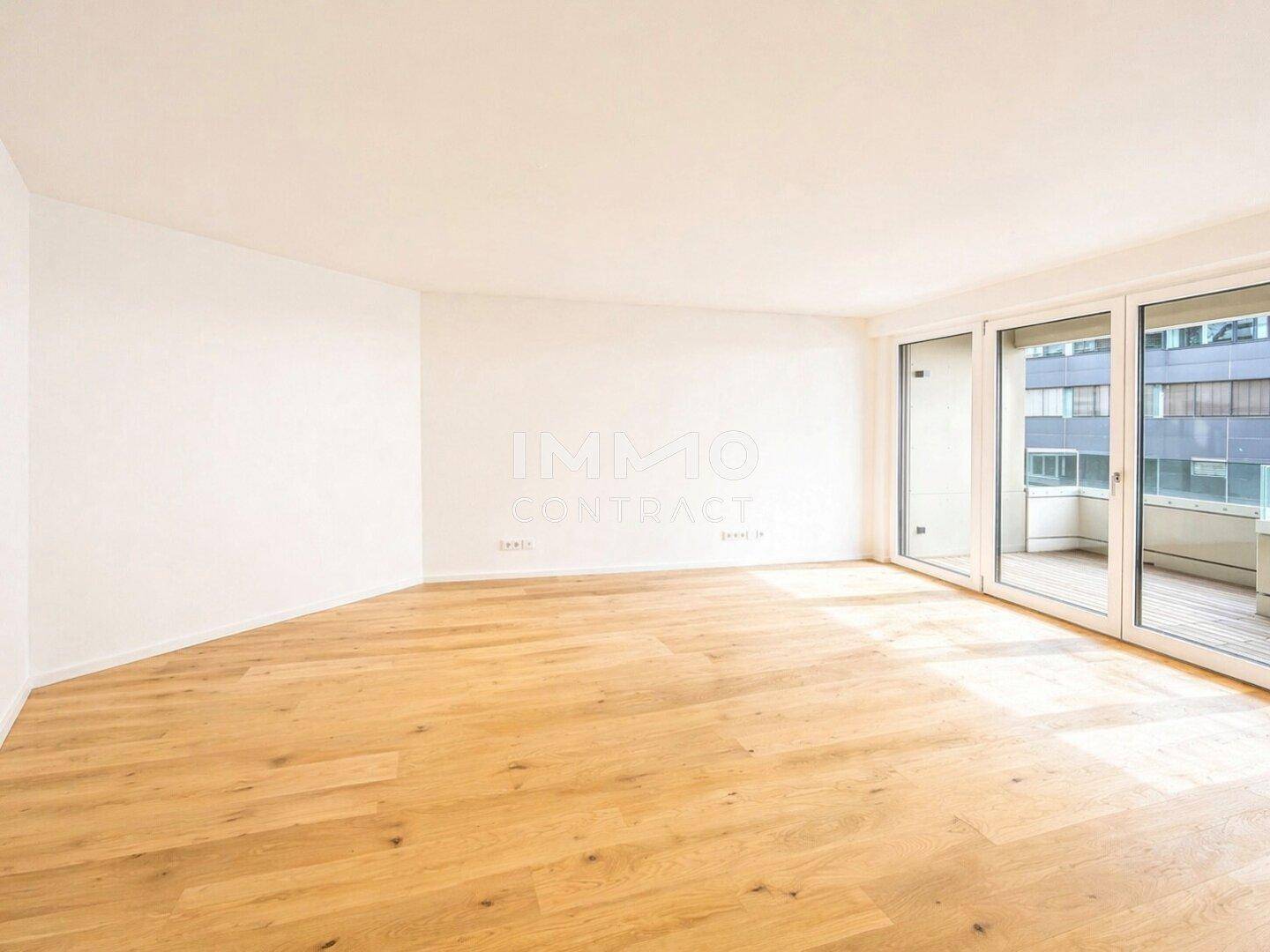 Lichtdurchfluteter Raum mit Holzboden und großen Fenstern, die viel Tageslicht hereinlassen.
