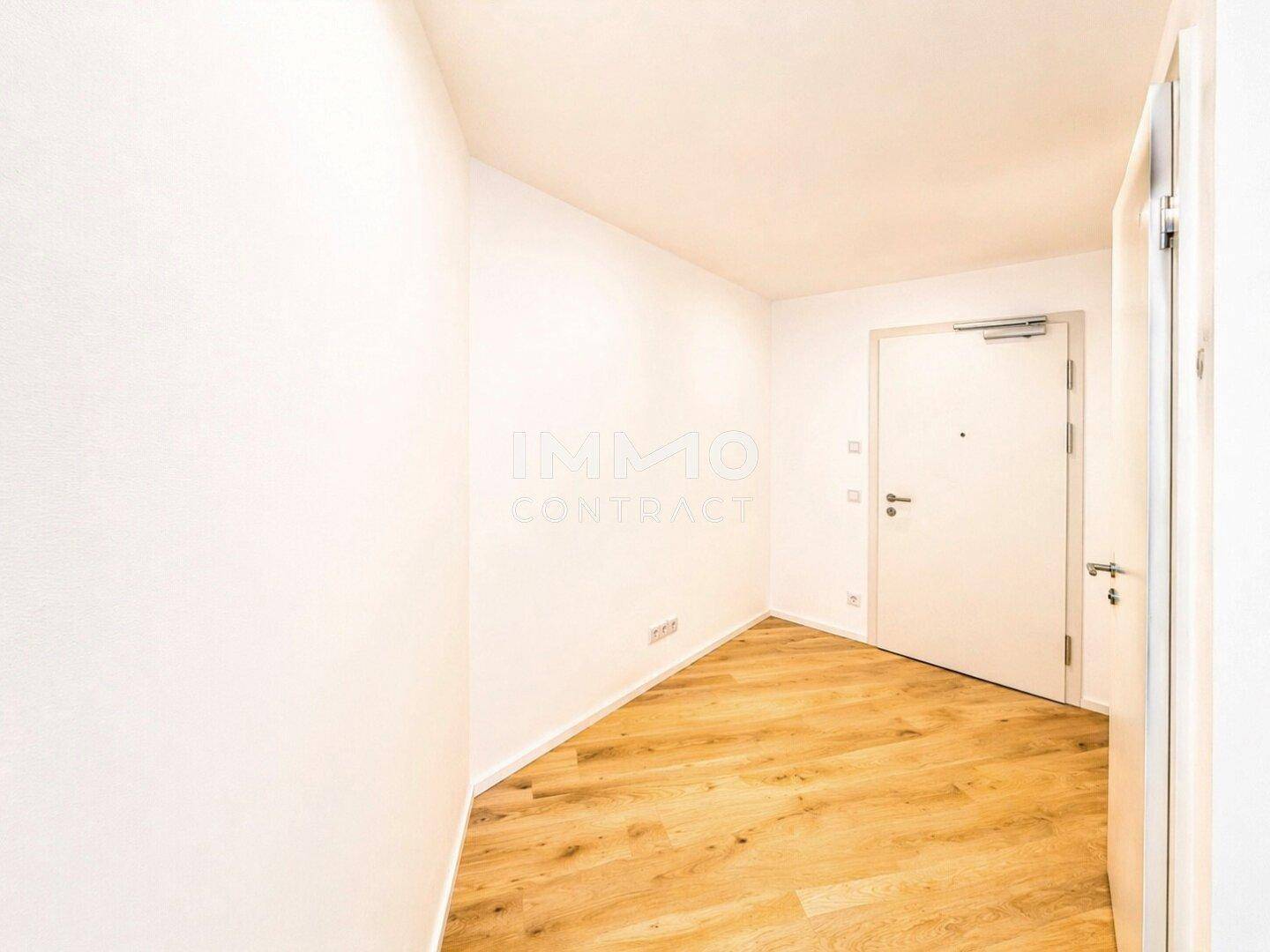 Heller Eingangsbereich mit Holzboden und weiß gestrichenen Wänden, führt zur Wohnungstür.