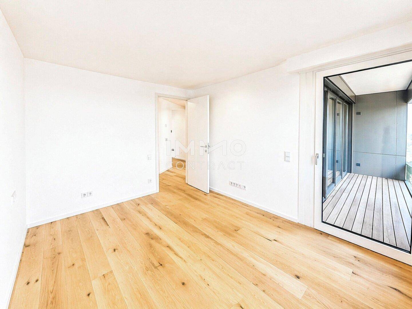Helles Zimmer mit Holzboden und Zugang zu einem Balkon, ideal als Schlaf- oder Arbeitszimmer.