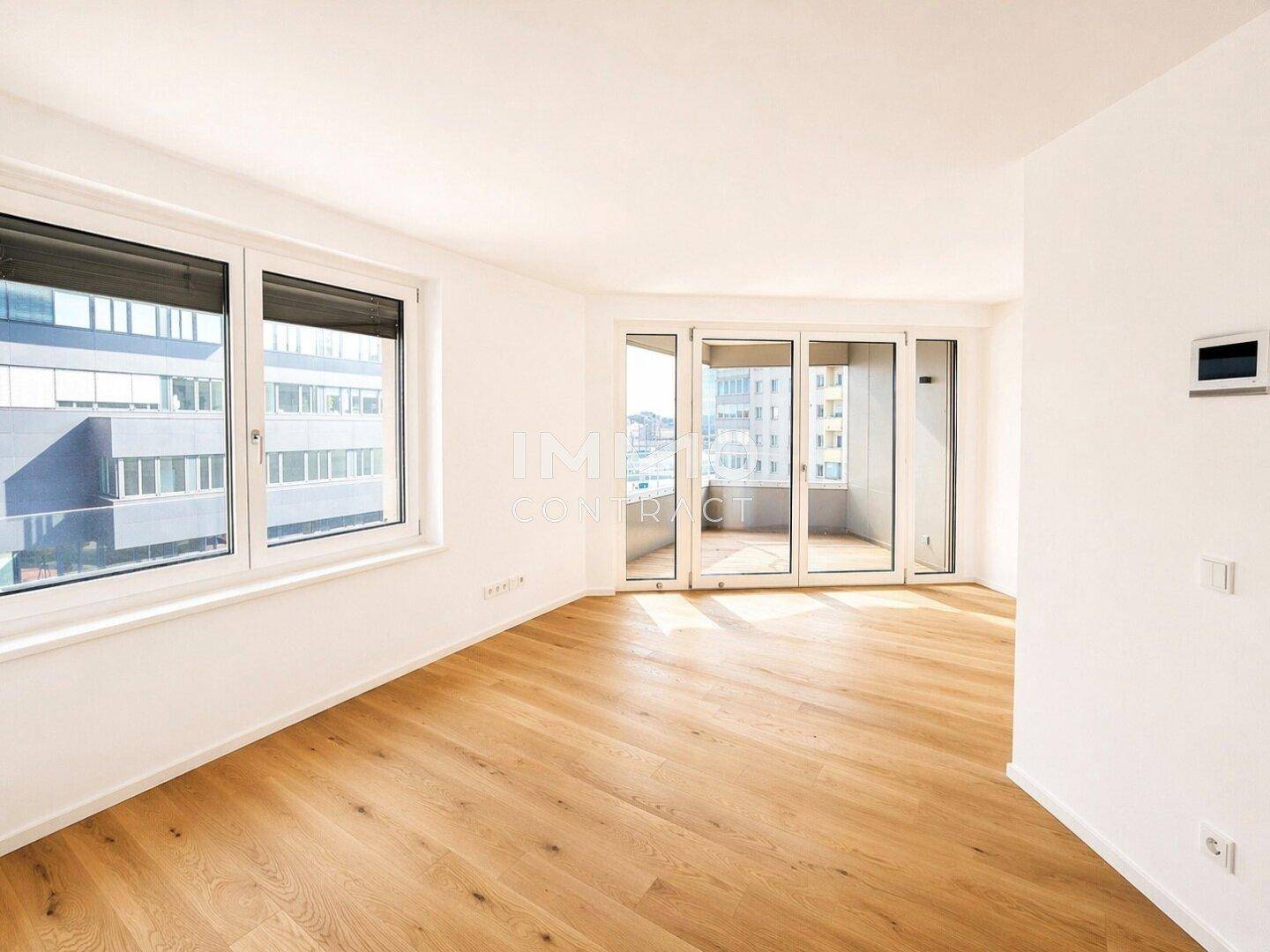 Geräumiges Wohnzimmer mit hellem Holzparkett, großen Fenstern und direktem Zugang zum Balkon.