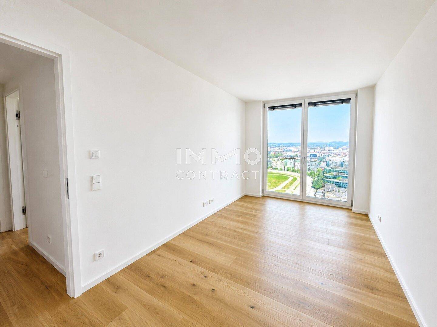 Geräumiges Schlafzimmer mit Holzboden und großem Fenster, das einen weiten Blick auf die Stadt bietet.