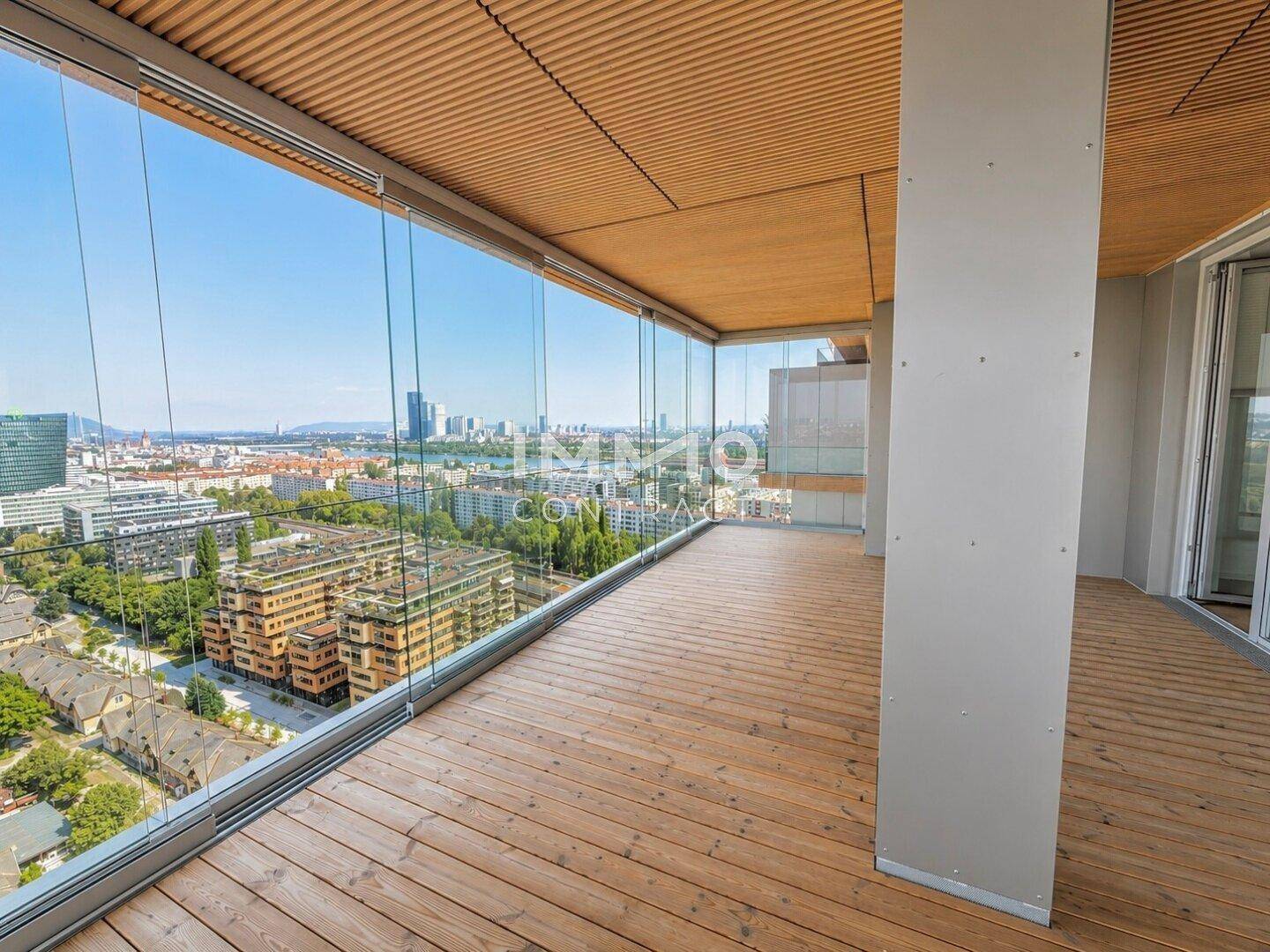 Helle Loggia mit Holzboden, Glasbrüstung und weitem Blick auf die umliegenden Gebäude und die Stadt.