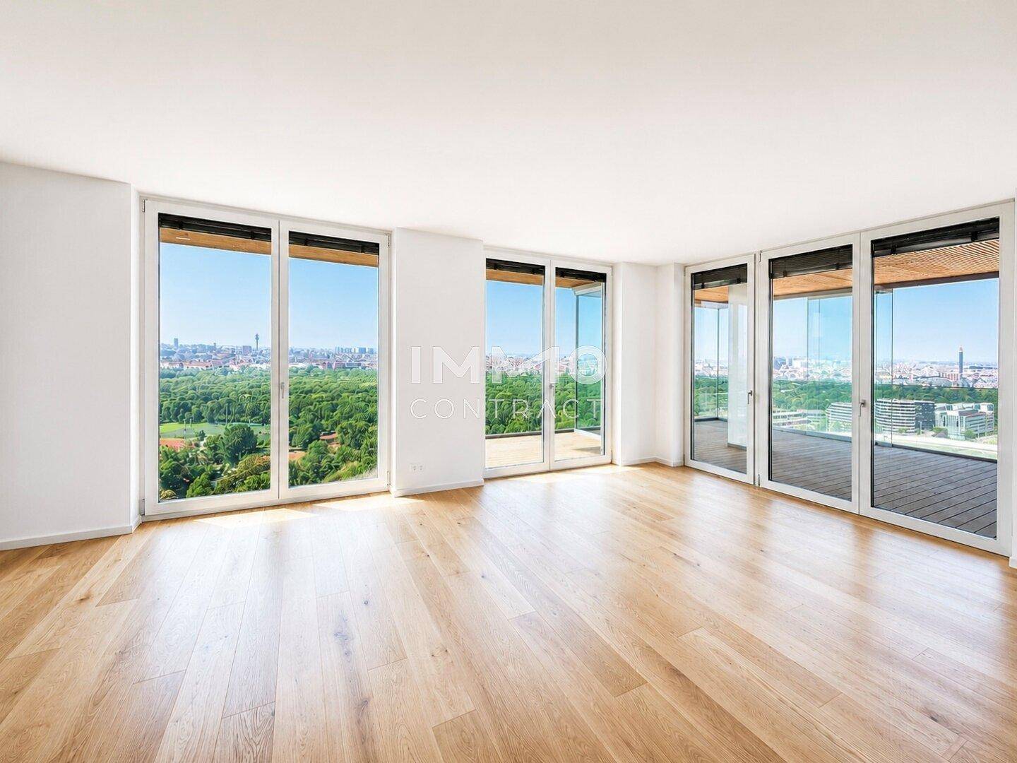 Geräumiges Wohnzimmer mit hellem Holzboden und raumhohen Fenstern mit Stadt- und Grünblick.