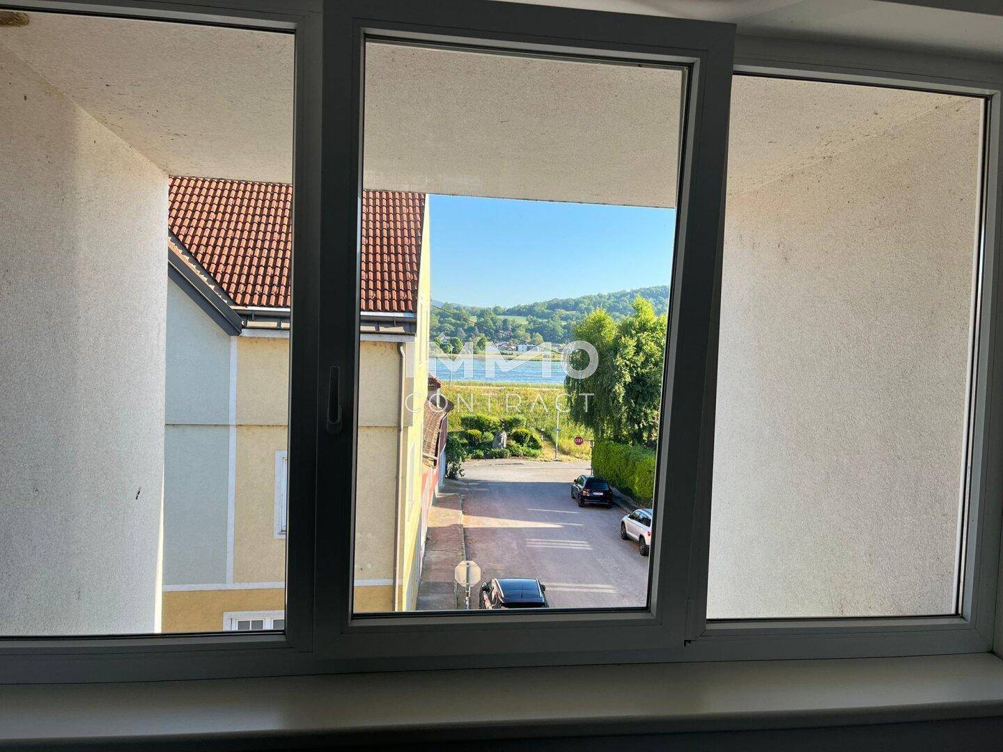 Ausblick aus einem Fenster auf eine Straße, Häuser, Bäume und einen See in der Ferne.