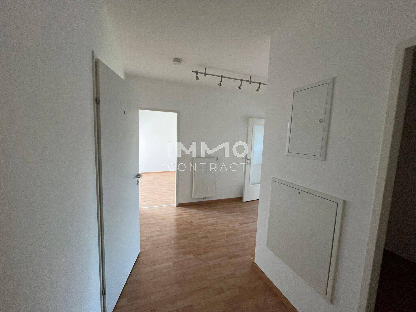Heller Flur mit Holzboden und weißen Wänden, der zu verschiedenen Räumen der Wohnung führt.