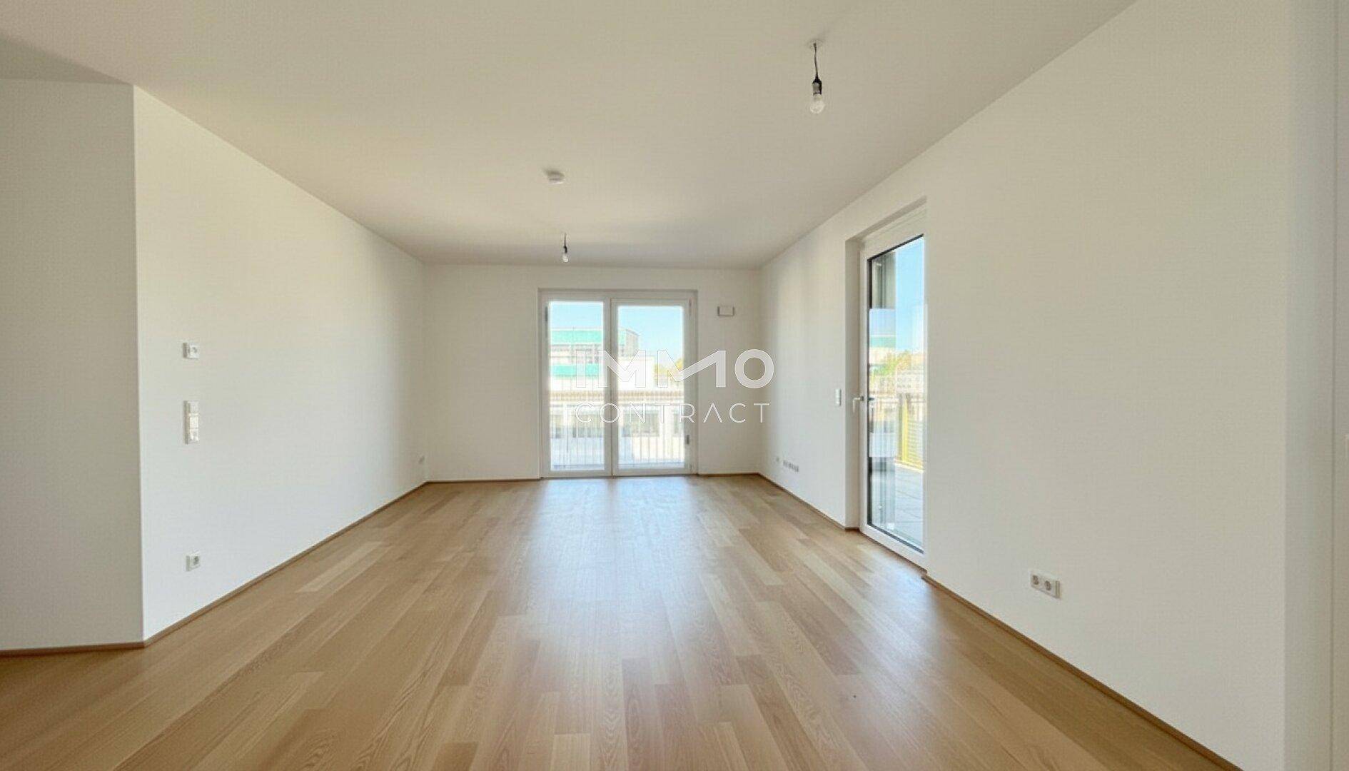 Heller, unmöblierter Wohnraum mit Parkettboden und Zugang zu einem Balkon.