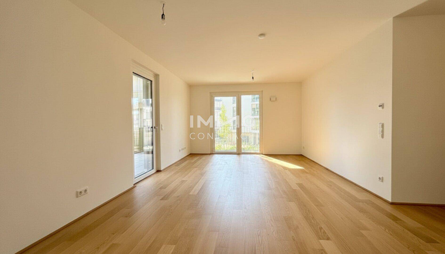 Helles, leeres Zimmer mit Holzboden und Zugang zu einem Balkon oder einer Terrasse.