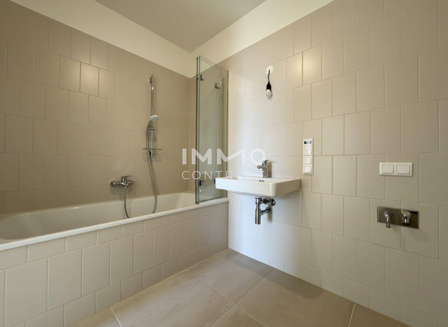 Modernes Badezimmer mit beigefarbenen Fliesen, Badewanne mit Duschwand und Einzelwaschbecken.