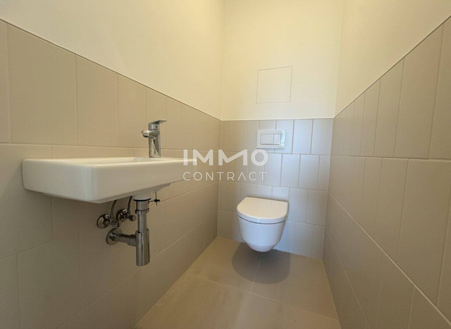 Separates Gäste-WC mit wandhängender Toilette und kleinem Waschbecken, hell gefliest.