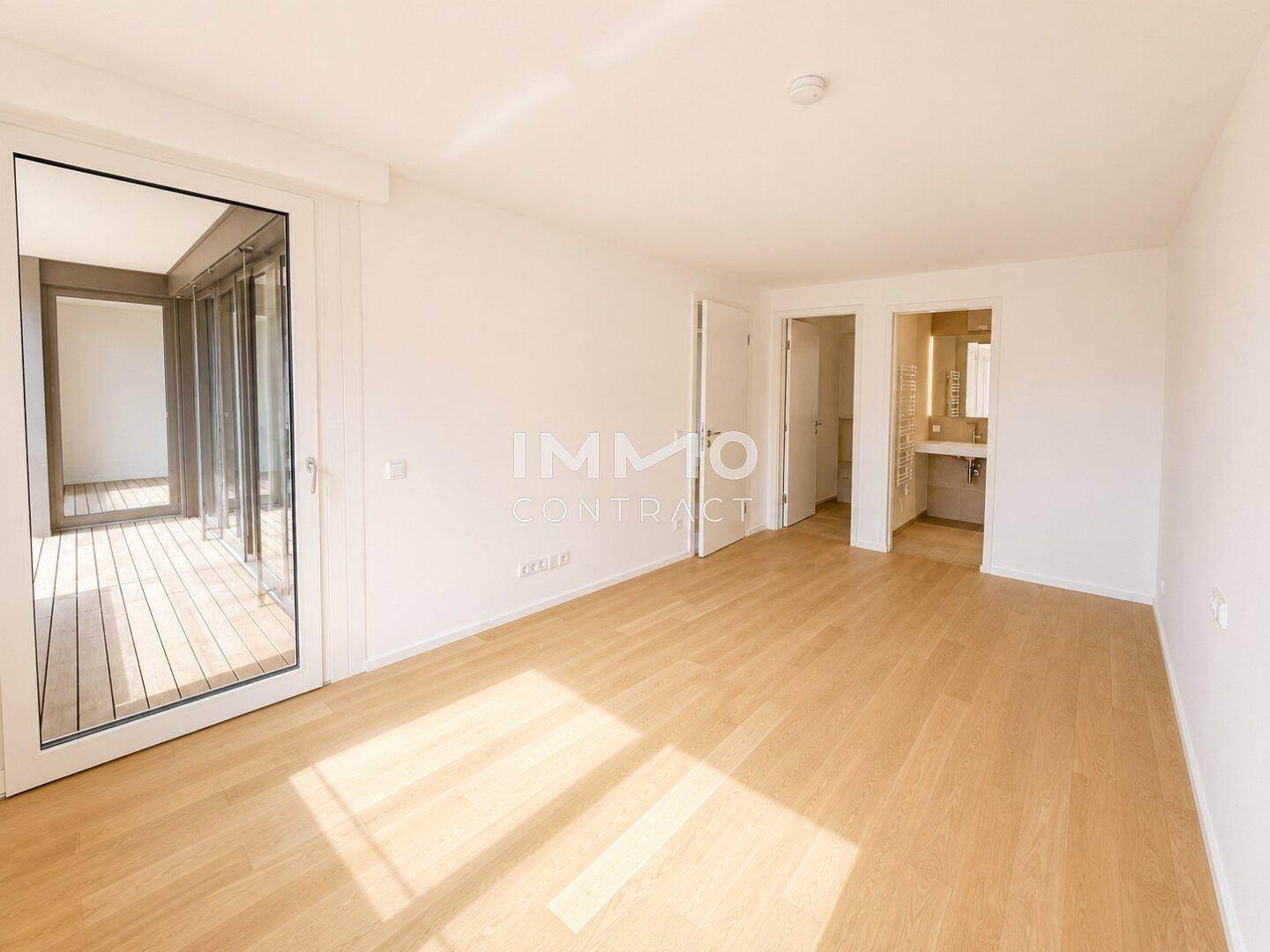 Helles Schlafzimmer mit Holzboden und Zugang zu einem Balkon sowie einem angrenzenden Badezimmer.
