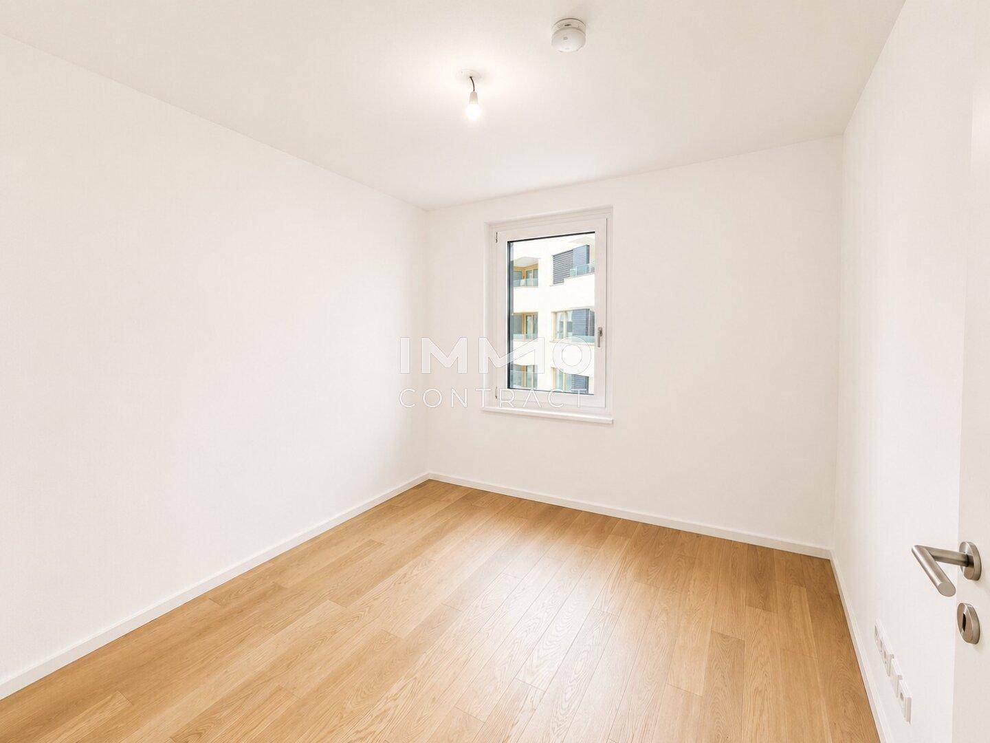 Schlichtes Schlafzimmer mit Holzboden und einem Fenster, das einen Blick nach draußen bietet.
