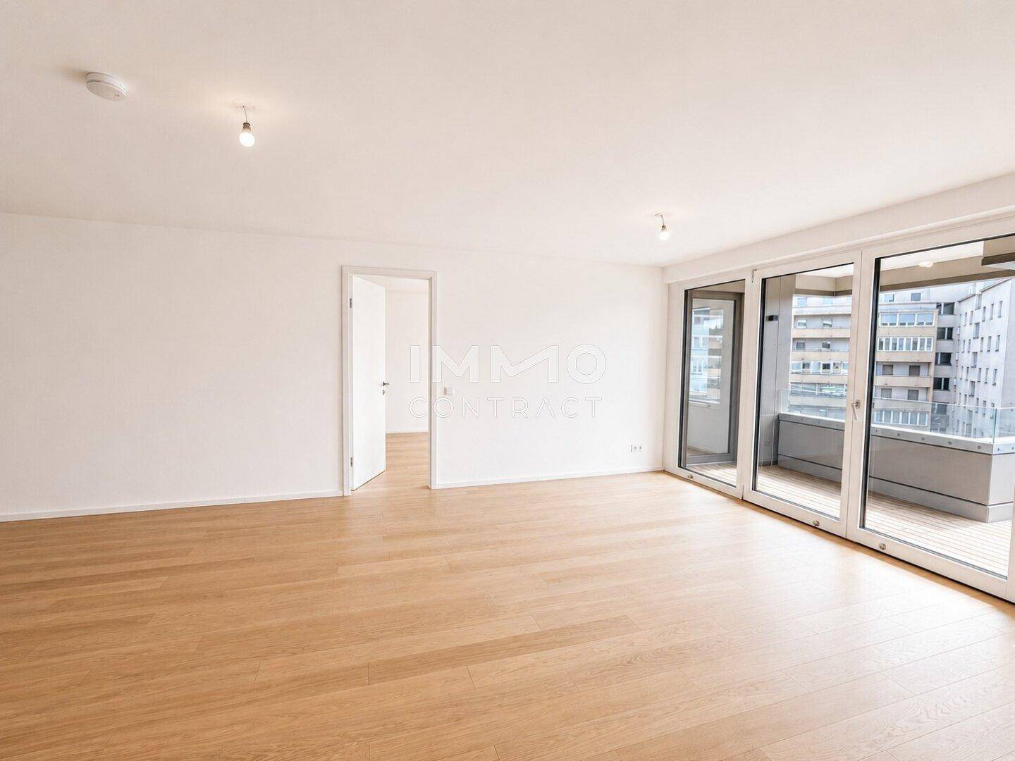 Geräumiger, heller Wohnbereich mit Holzboden und großen Schiebetüren zum Balkon.