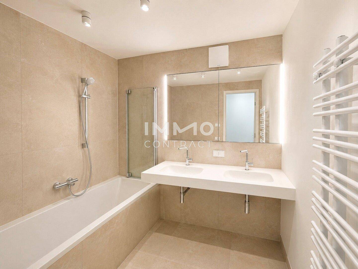 Modernes Badezimmer mit Doppelwaschbecken, Badewanne mit Duschfunktion und beheiztem Handtuchhalter.