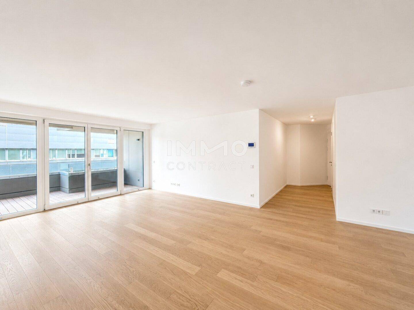 Helles Wohnzimmer mit Parkettboden und großen Glasfronten zum Balkon.